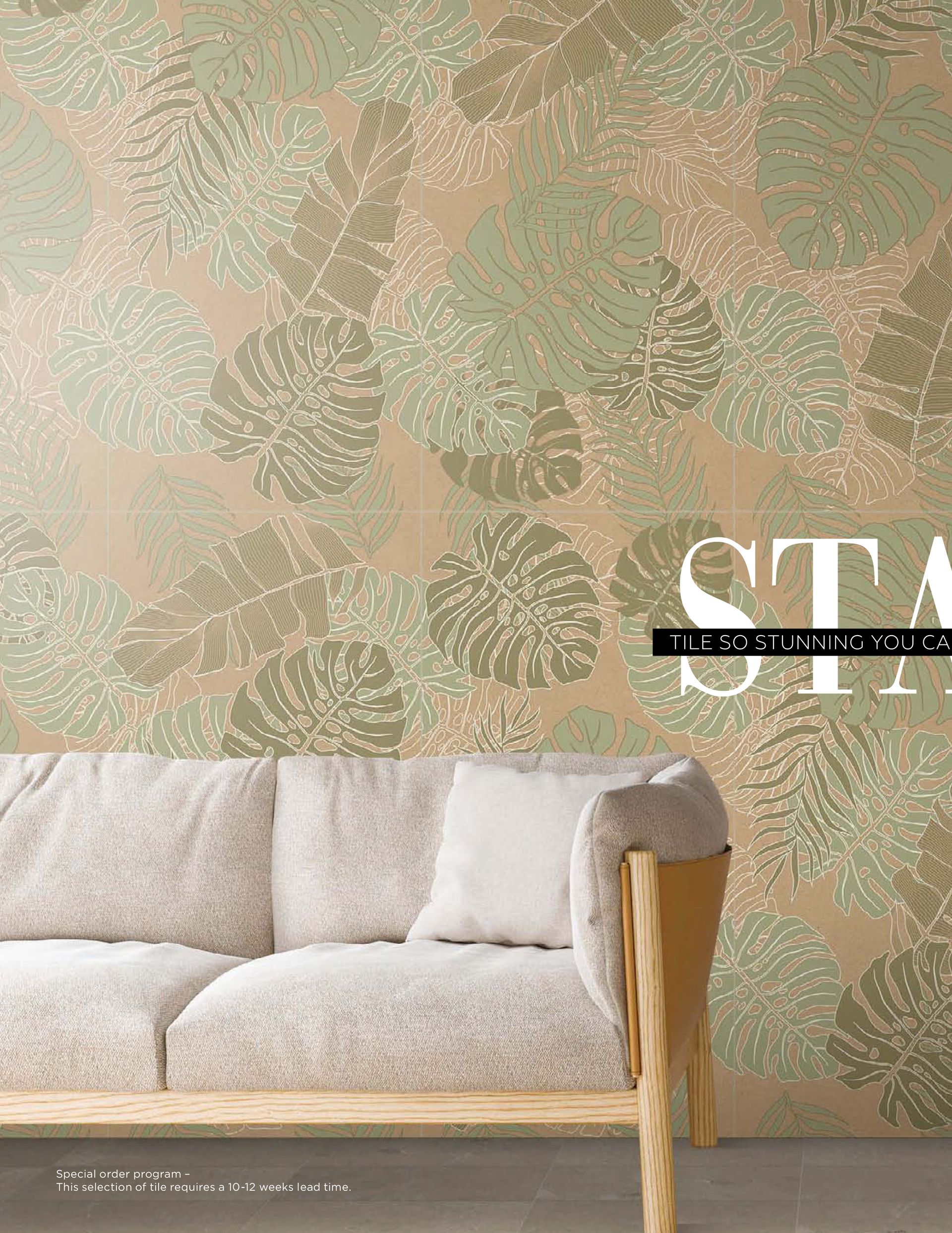 A couch is sitting in front of a wall with leaves on it.