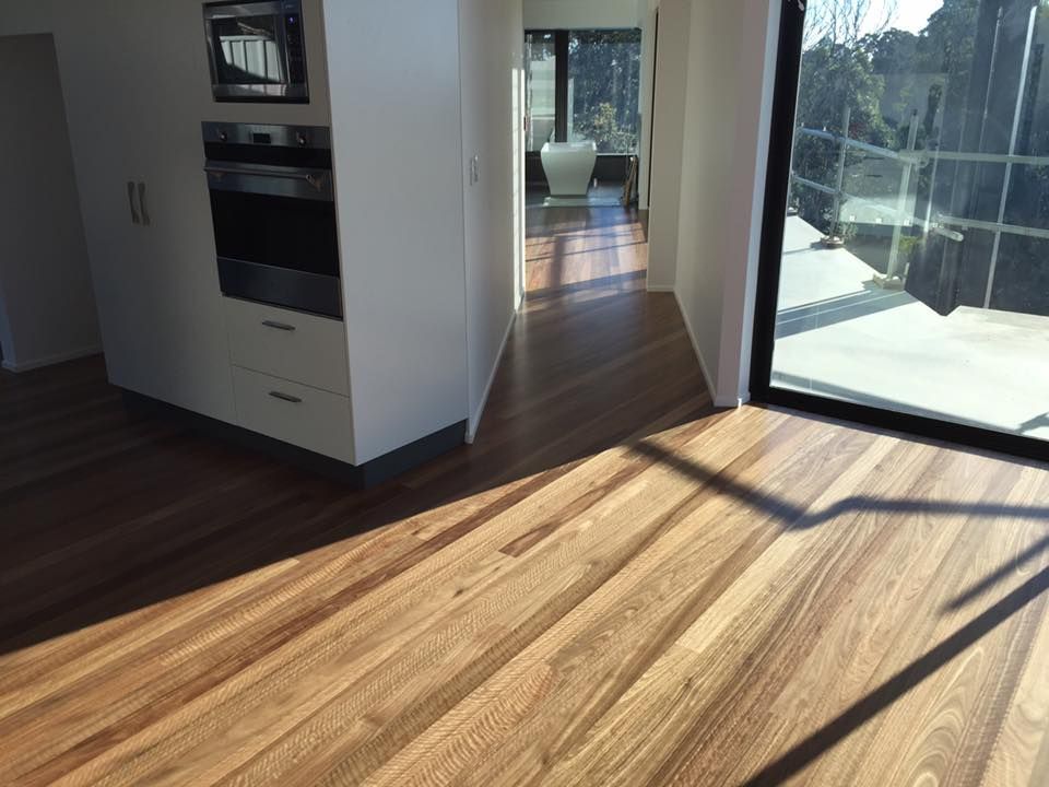 Wooden floors in a modern home, with a hallway, kitchen cabinetry, and large window casting sunlight — CM Timber Flooring in East Ballina, NSW