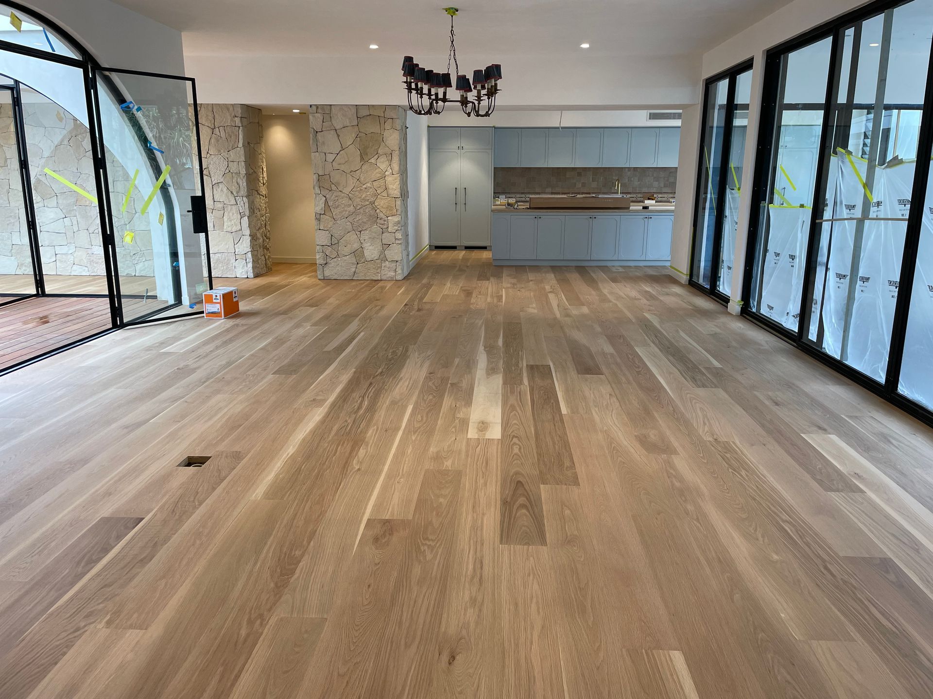 Empty room with light wood floors, glass walls and a blue kitchen in the background — CM Timber Flooring in East Ballina, NSW