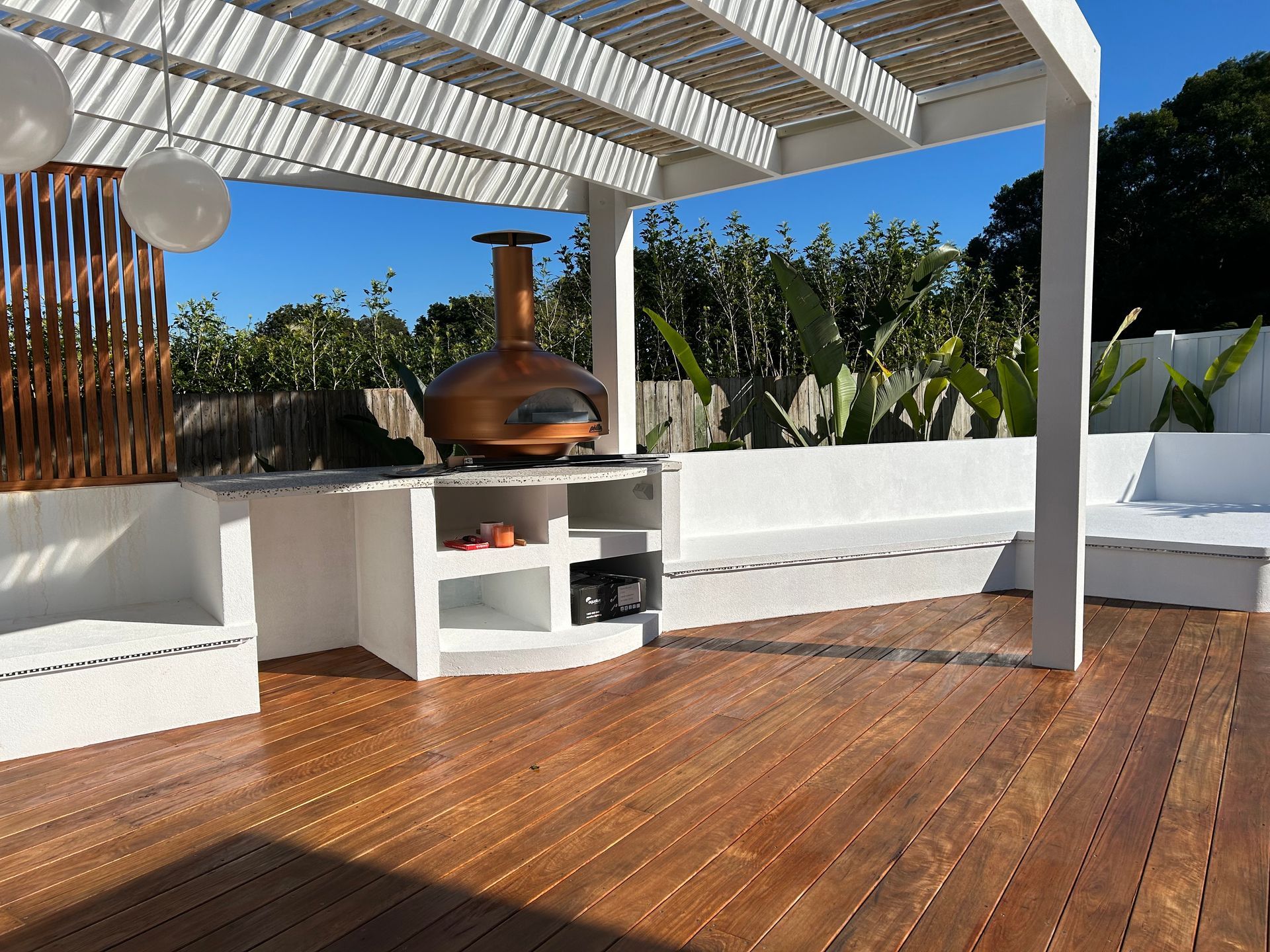 Wooden deck with white pergola, outdoor pizza oven, built-in bench seating, and lush greenery — CM Timber Flooring in East Ballina, NSW