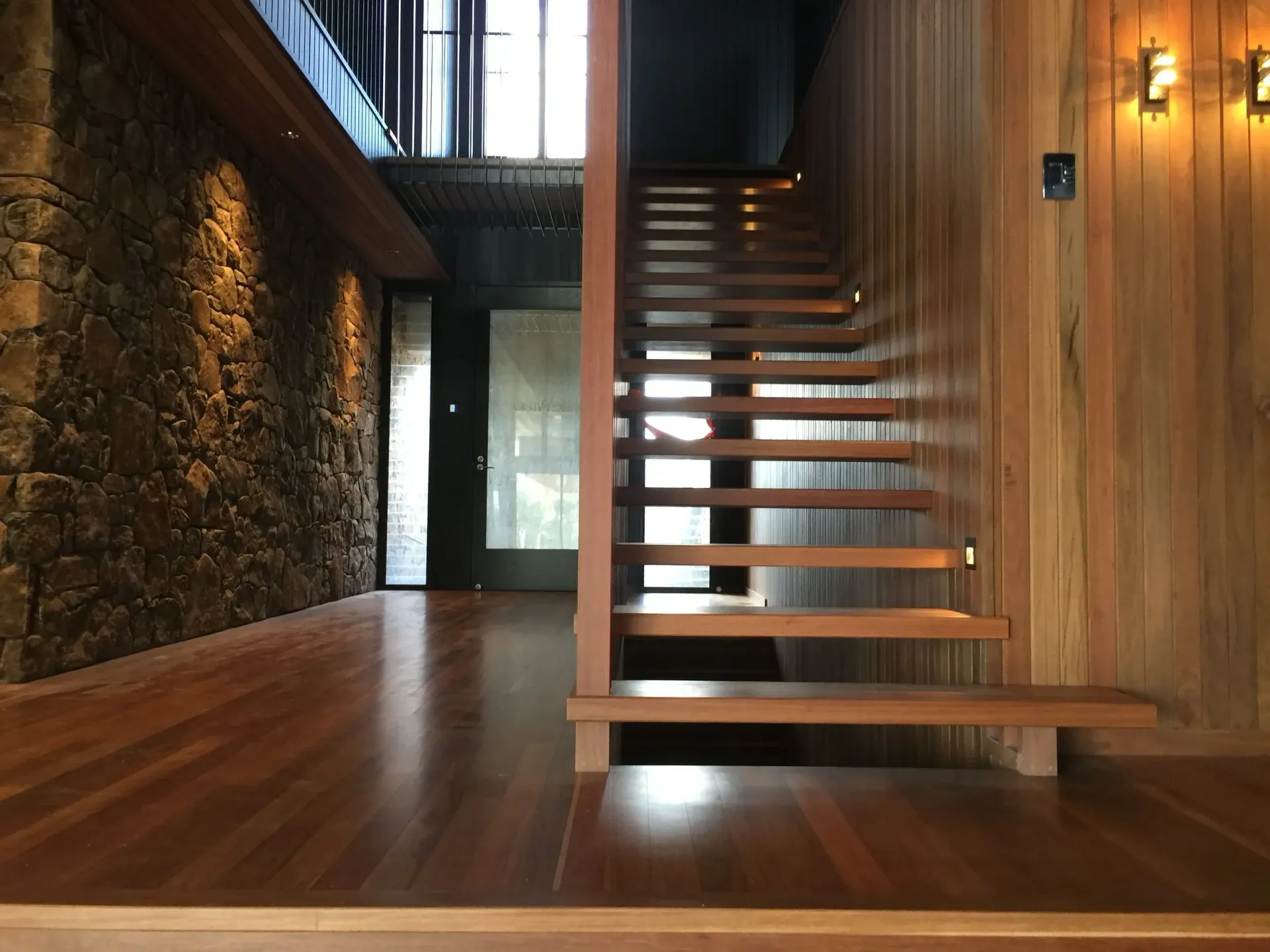 Wooden staircase in a home with stone wall and wood flooring, illuminated by warm lighting — CM Timber Flooring in East Ballina, NSW