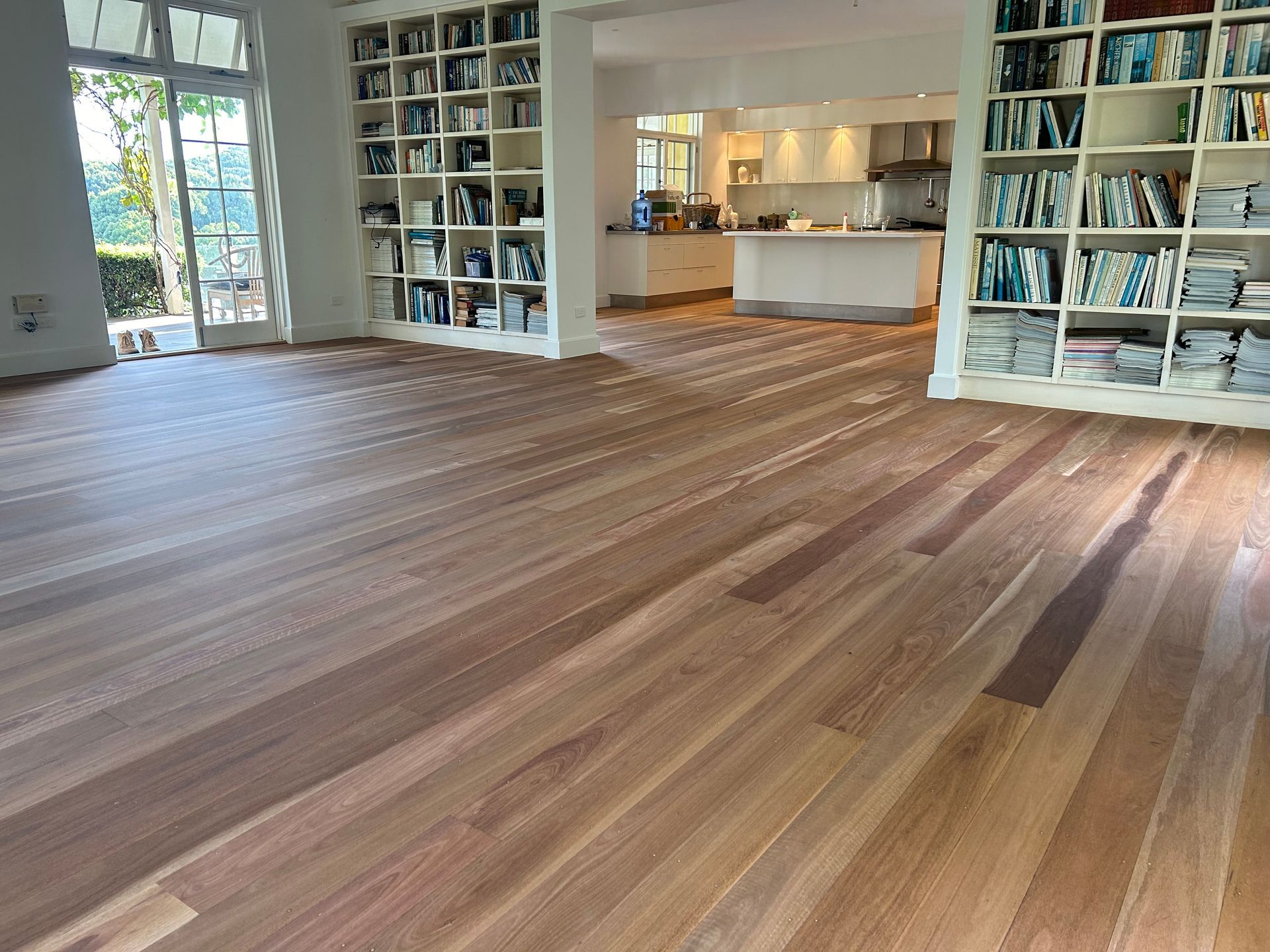 Hardwood floor in a spacious room, bookshelves in the background, a kitchen visible in the distance — CM Timber Flooring in East Ballina, NSW