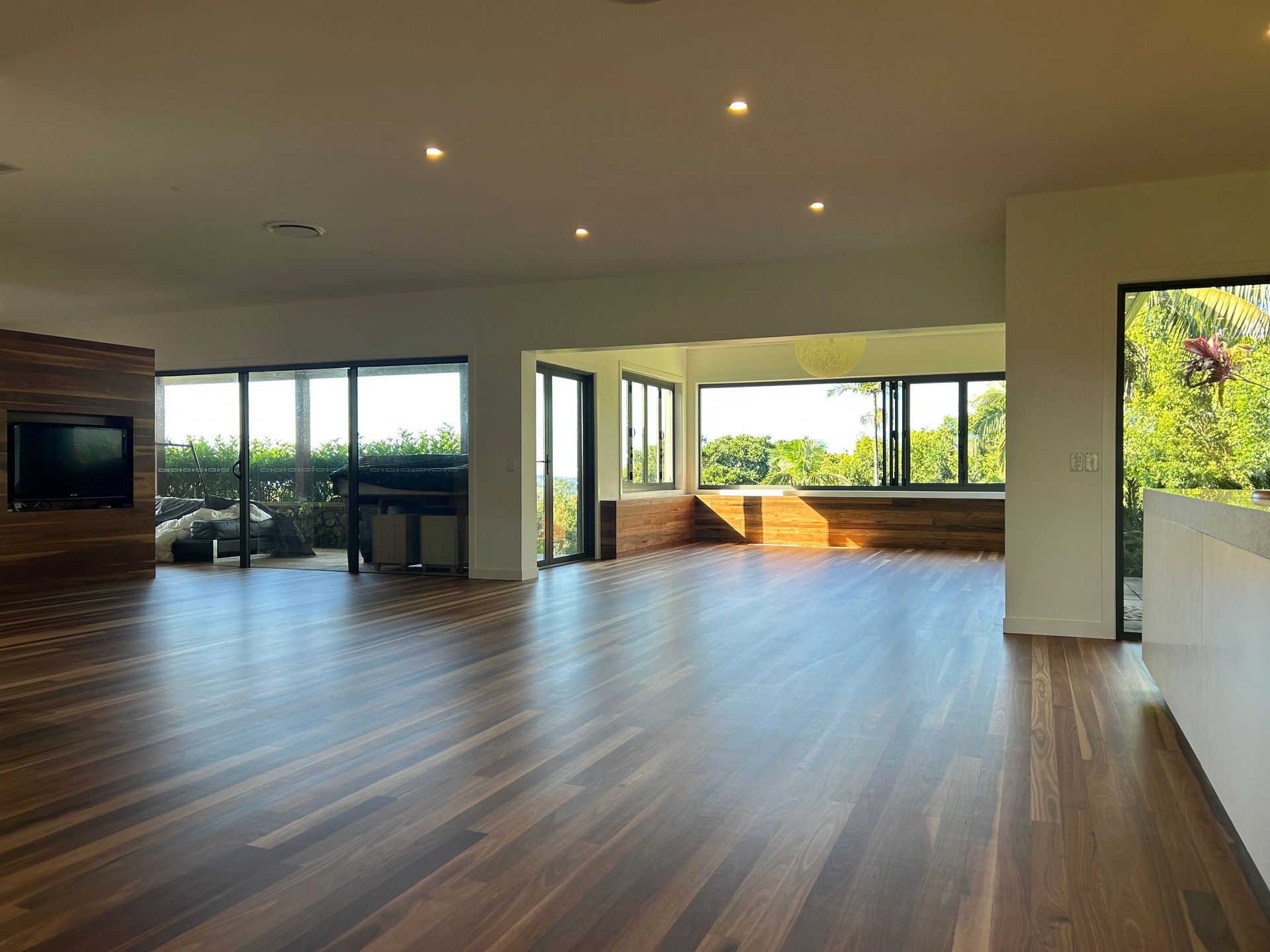Spacious living room with wood floors, large windows, and a built-in bench overlooking a green landscape — CM Timber Flooring in East Ballina, NSW