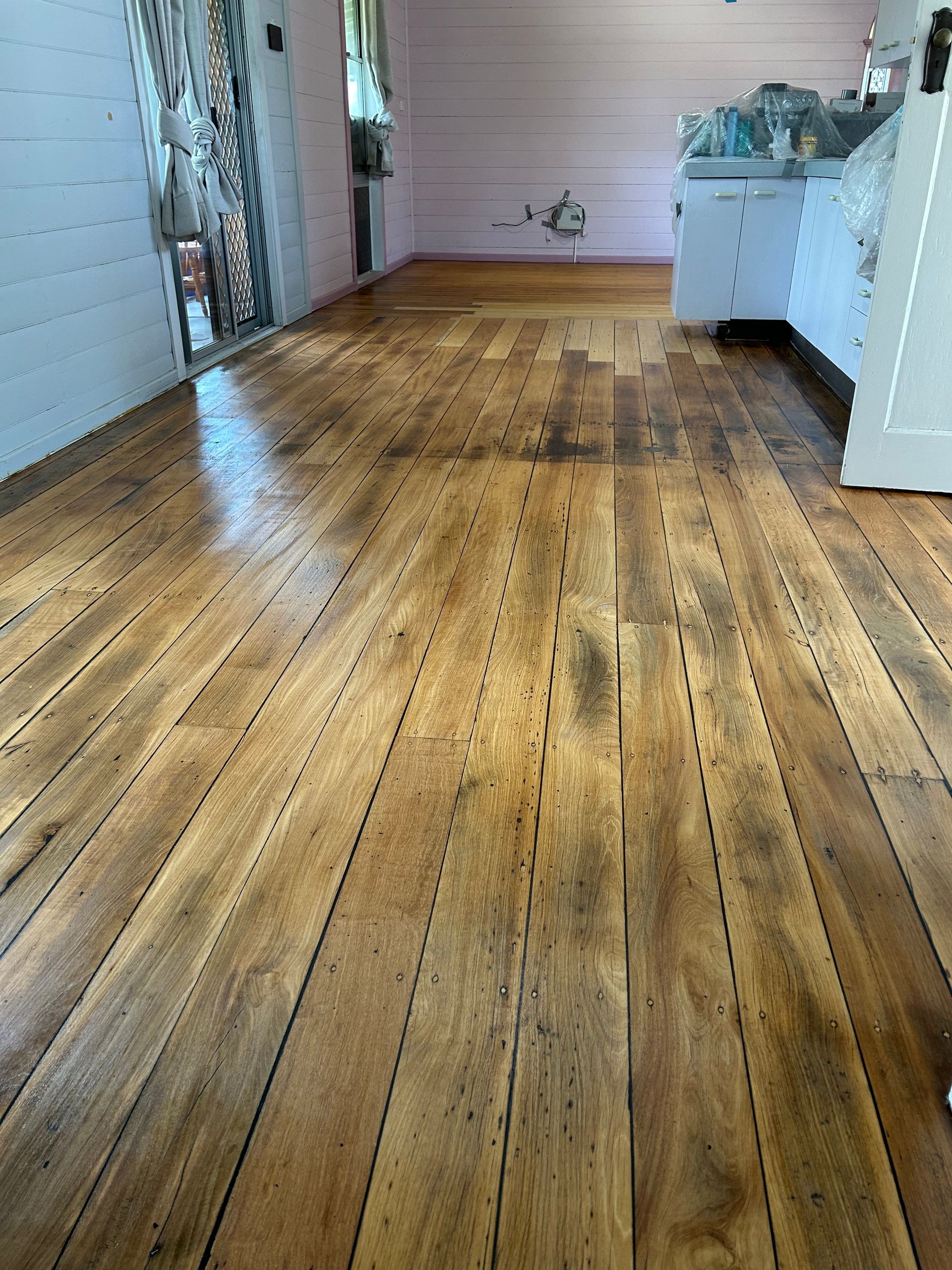 Wooden floor, well-worn, with varied light and dark brown tones; room with a white cabinet — CM Timber Flooring in East Ballina, NSW
