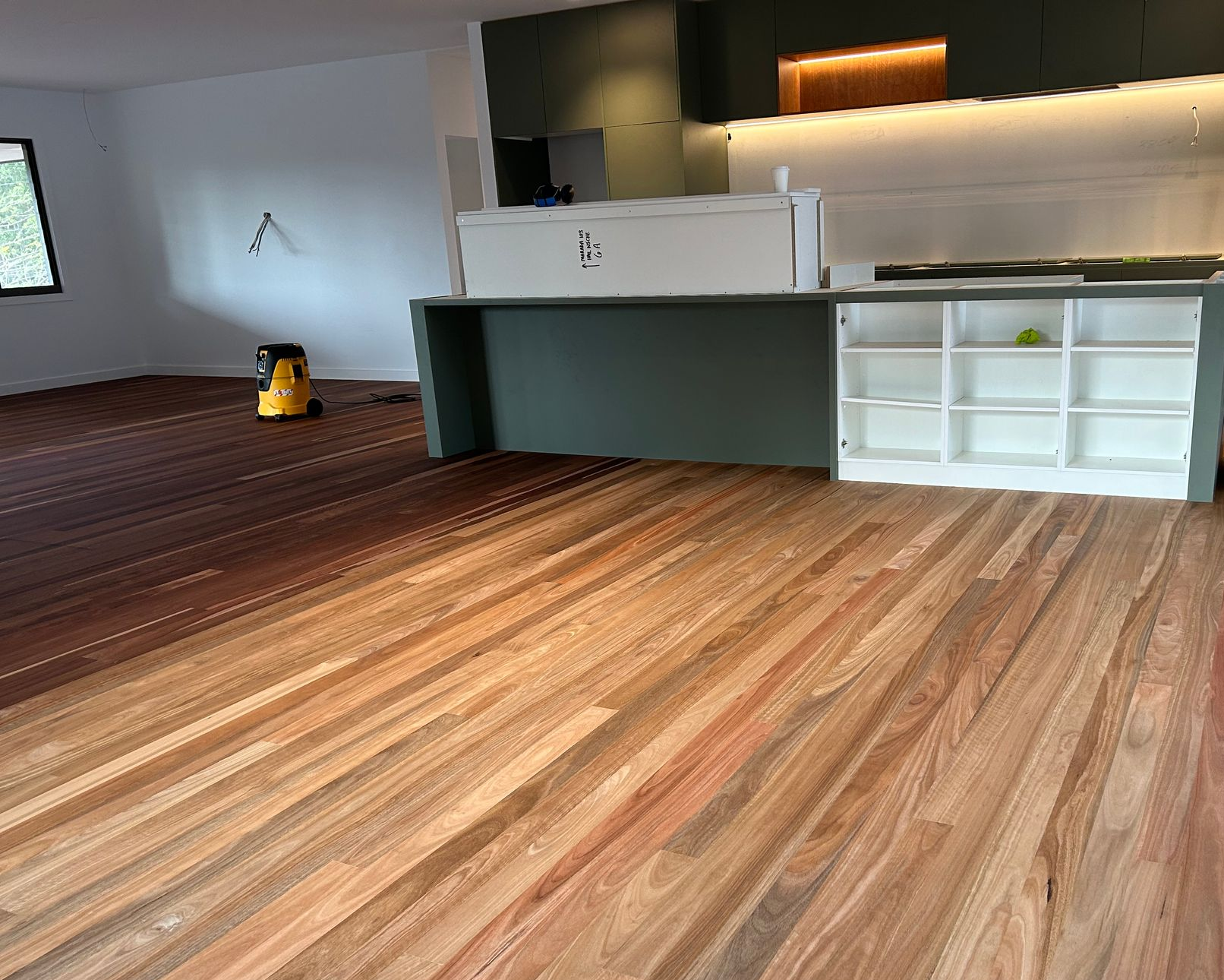 Hardwood floor being sanded, half stained dark brown, with kitchen island and cabinets — CM Timber Flooring in East Ballina, NSW