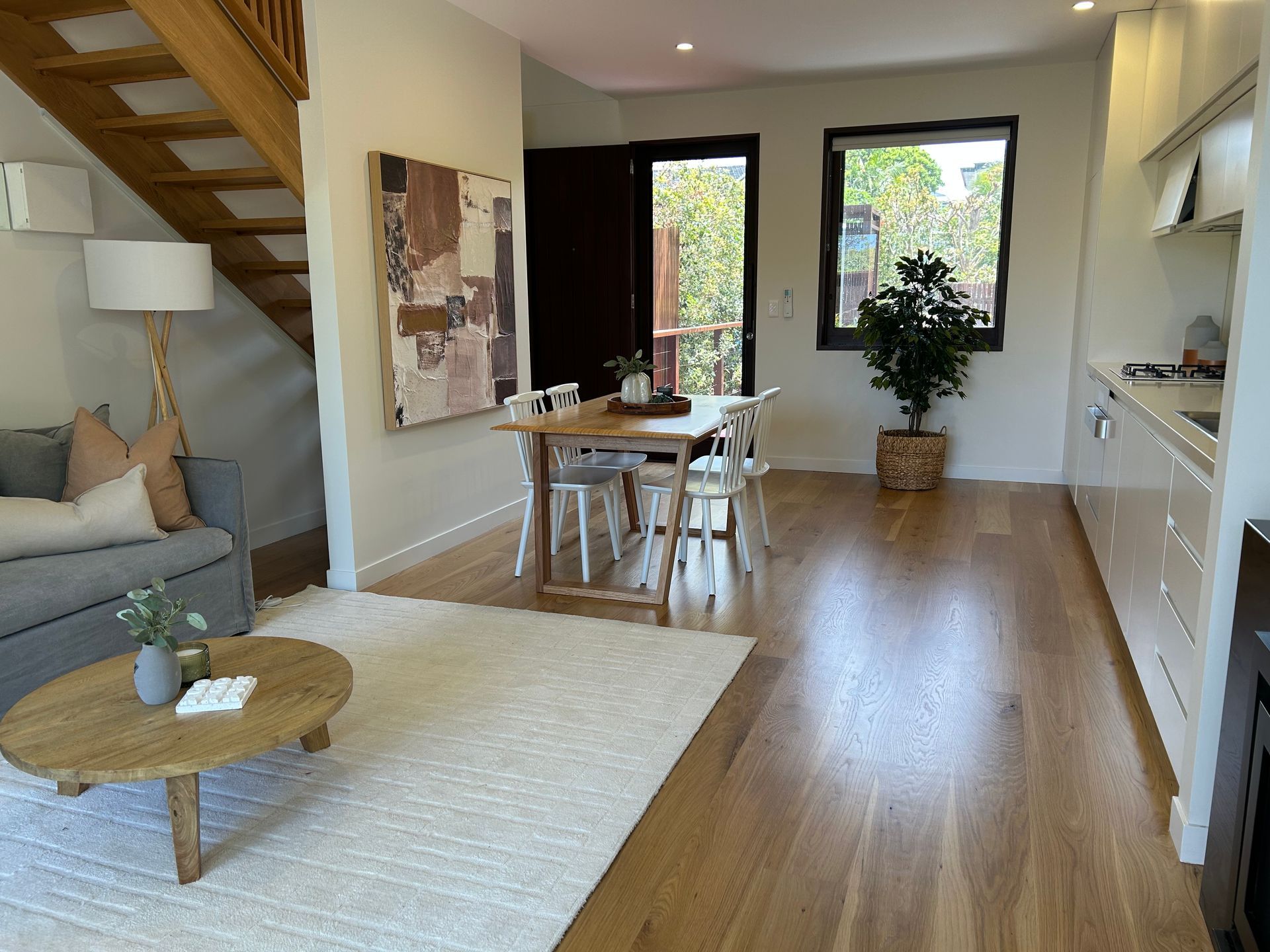 Living room with wooden floors, rug, sofa, table, chairs, art, stairs, and kitchen — CM Timber Flooring in East Ballina, NSW