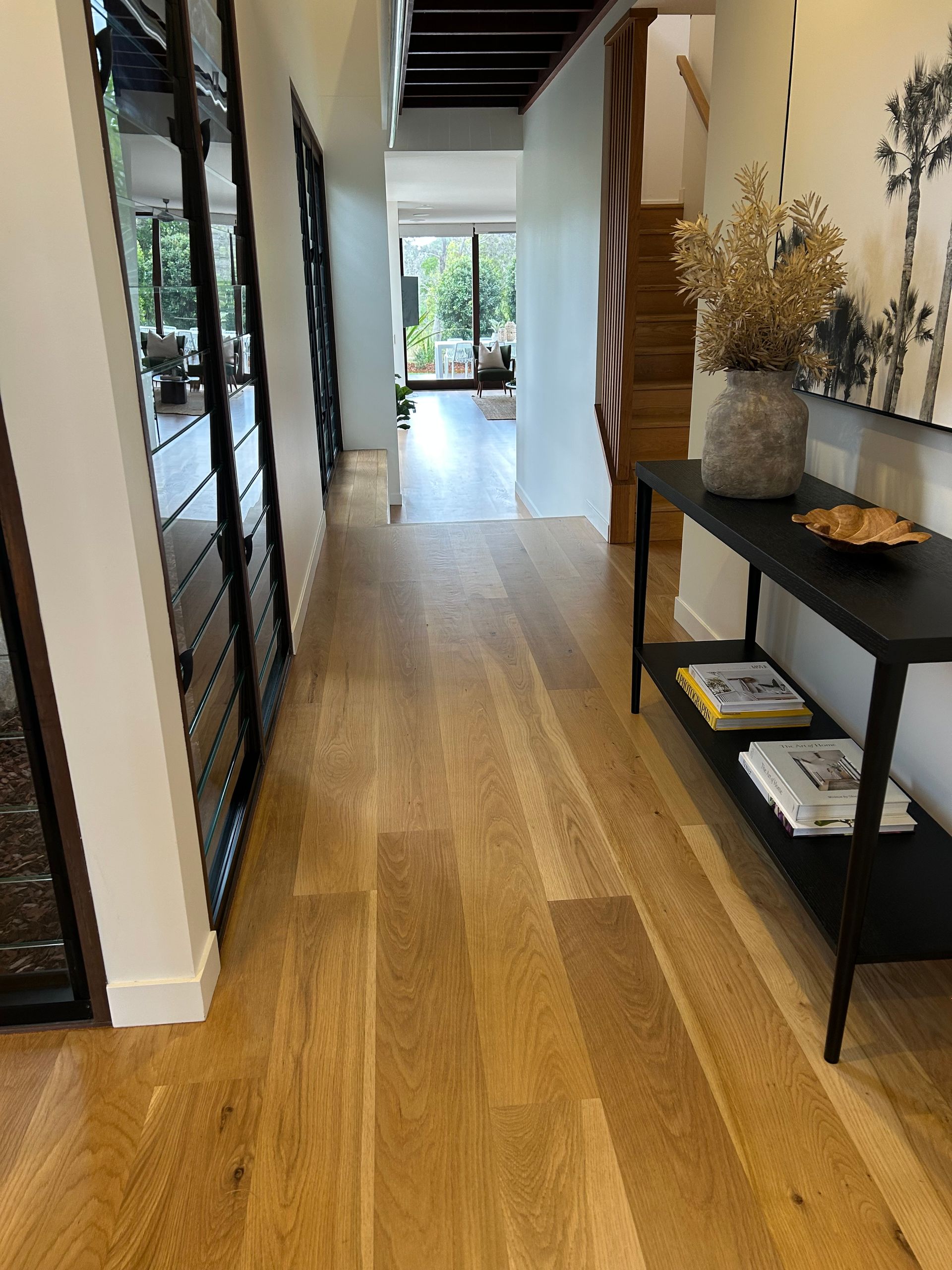 Hallway with wood floor, black console table with decor, and a staircase — CM Timber Flooring in East Ballina, NSW