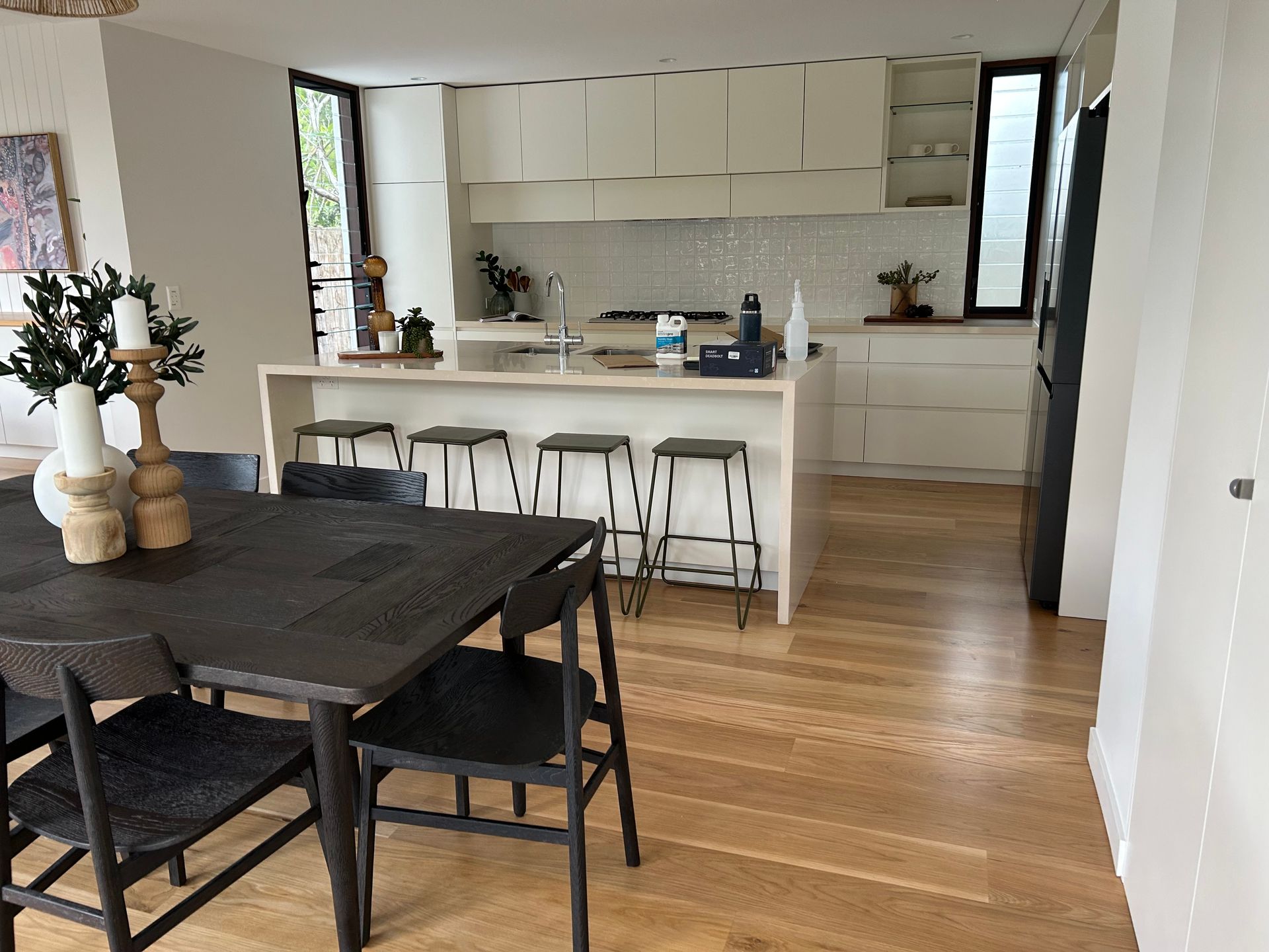 Dining area with dark table and chairs, light wood floor, and open kitchen with white cabinets — CM Timber Flooring in East Ballina, NSW