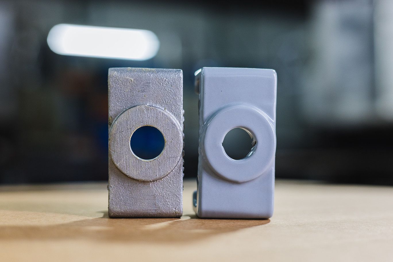 Two identical rectangular metal parts stand upright, one with a rough, unfinished grey surface and one with a smooth finish.