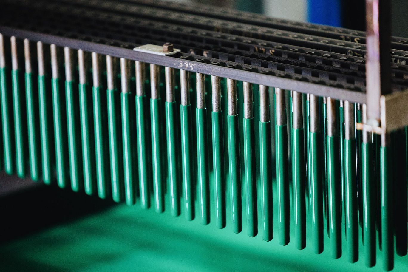 A row of green industrial rods hanging from a metallic frame above a green surface.