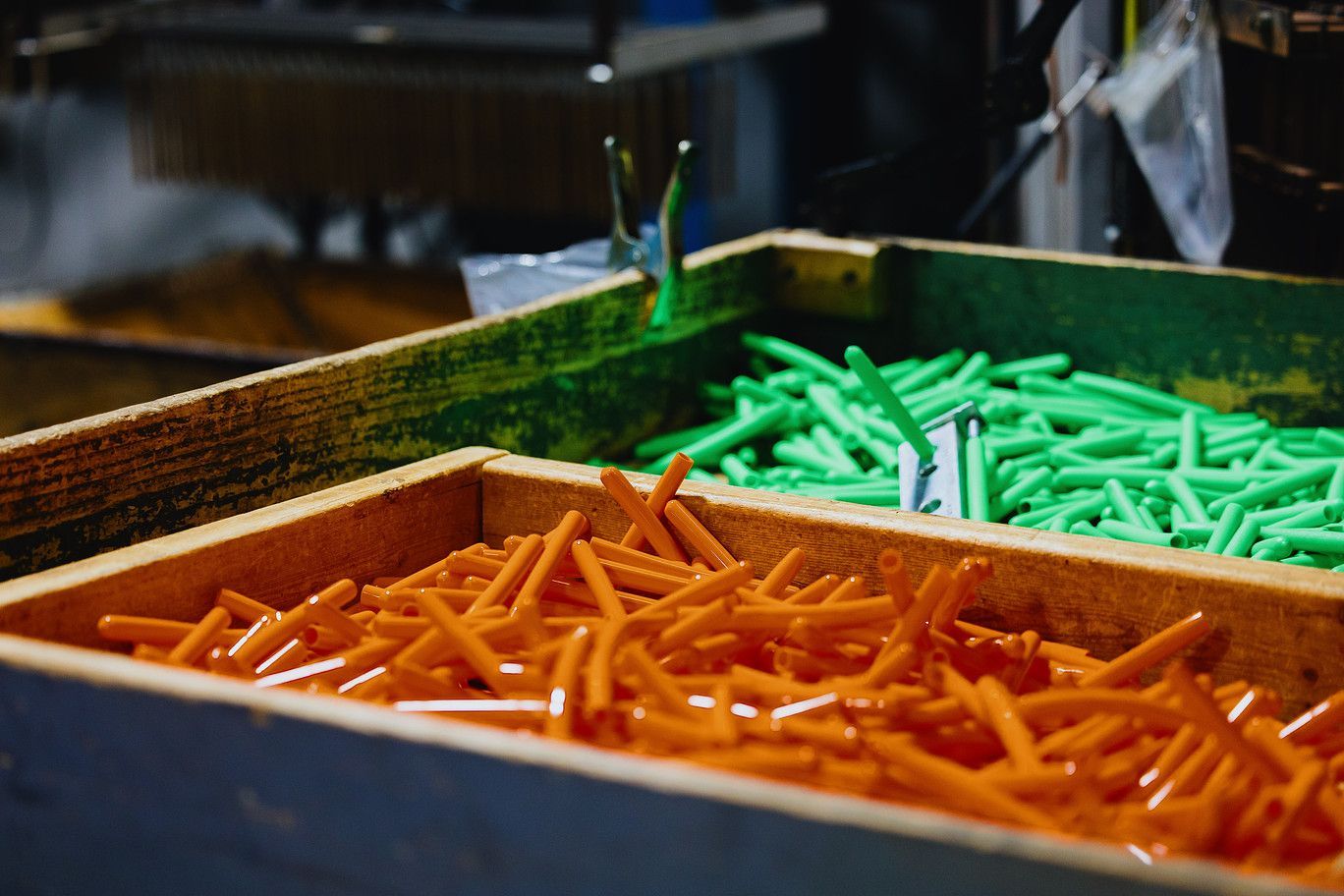 Two wooden bins filled with numerous orange and green plastic golf tees in a factory setting.