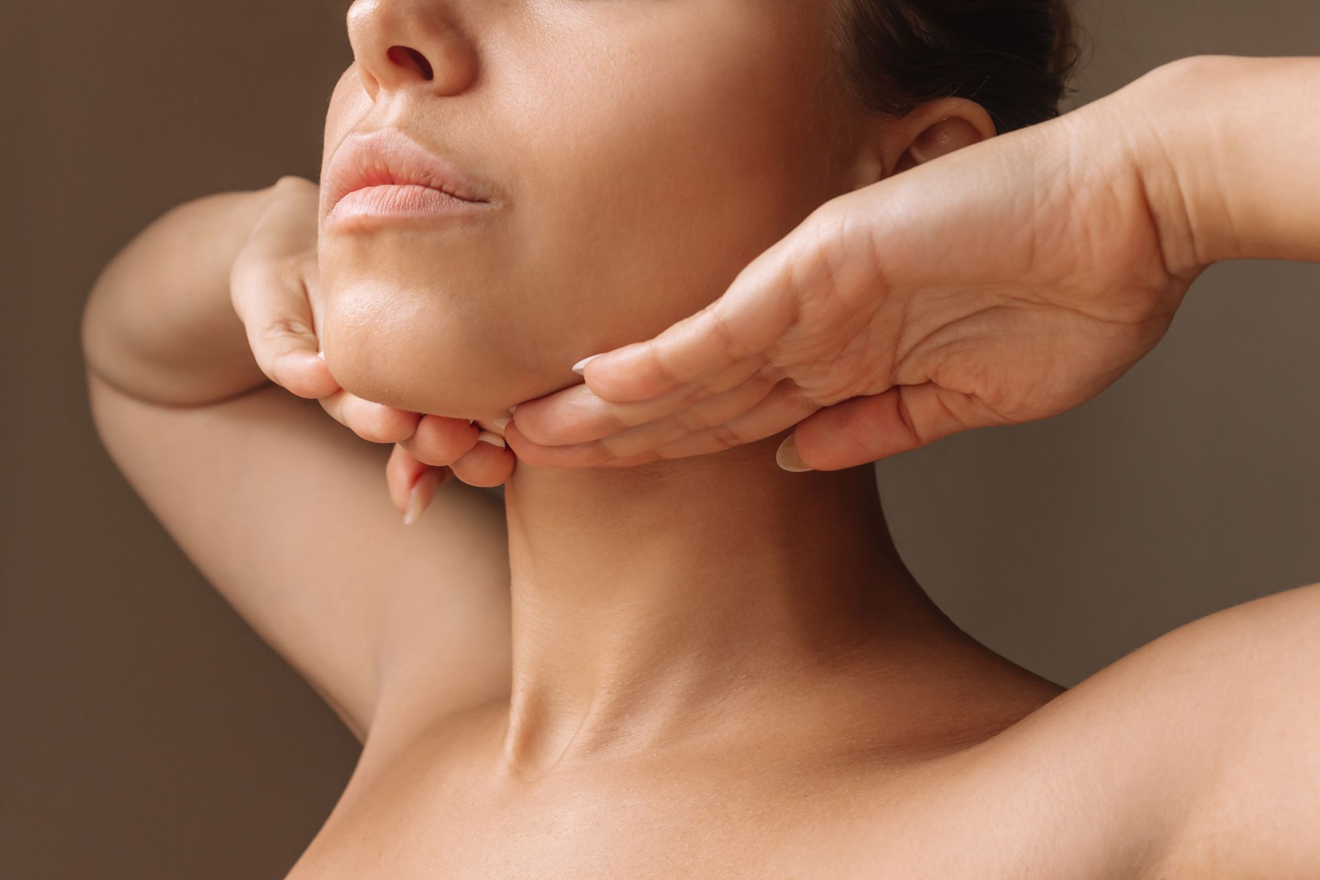 Hands gently massaging a woman's neck and jawline during a skincare or spa treatment.