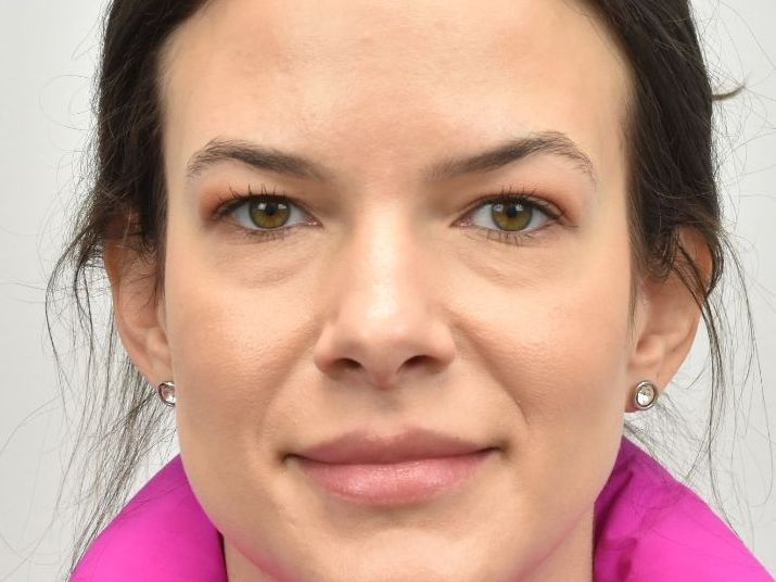 A woman wearing a pink jacket and earrings is smiling for the camera.