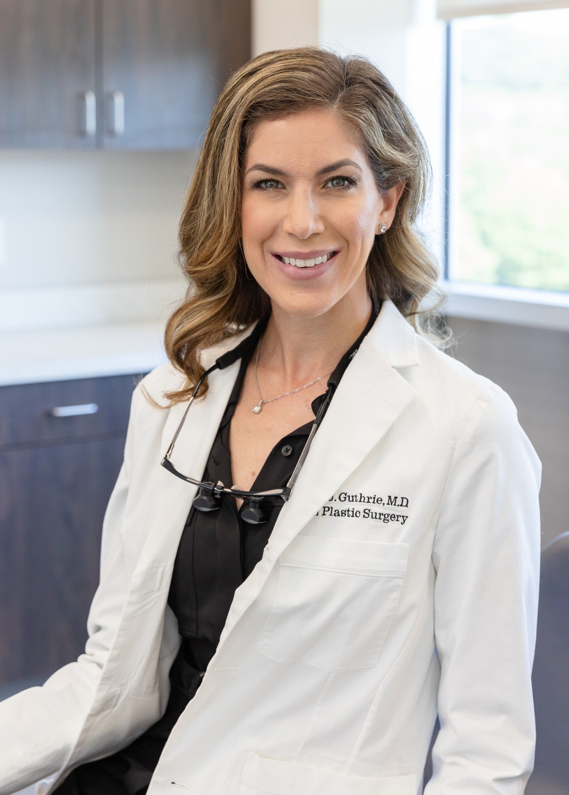 Dr. Ashley Guthrie in exam room, smiling and wearing white doctor's coat