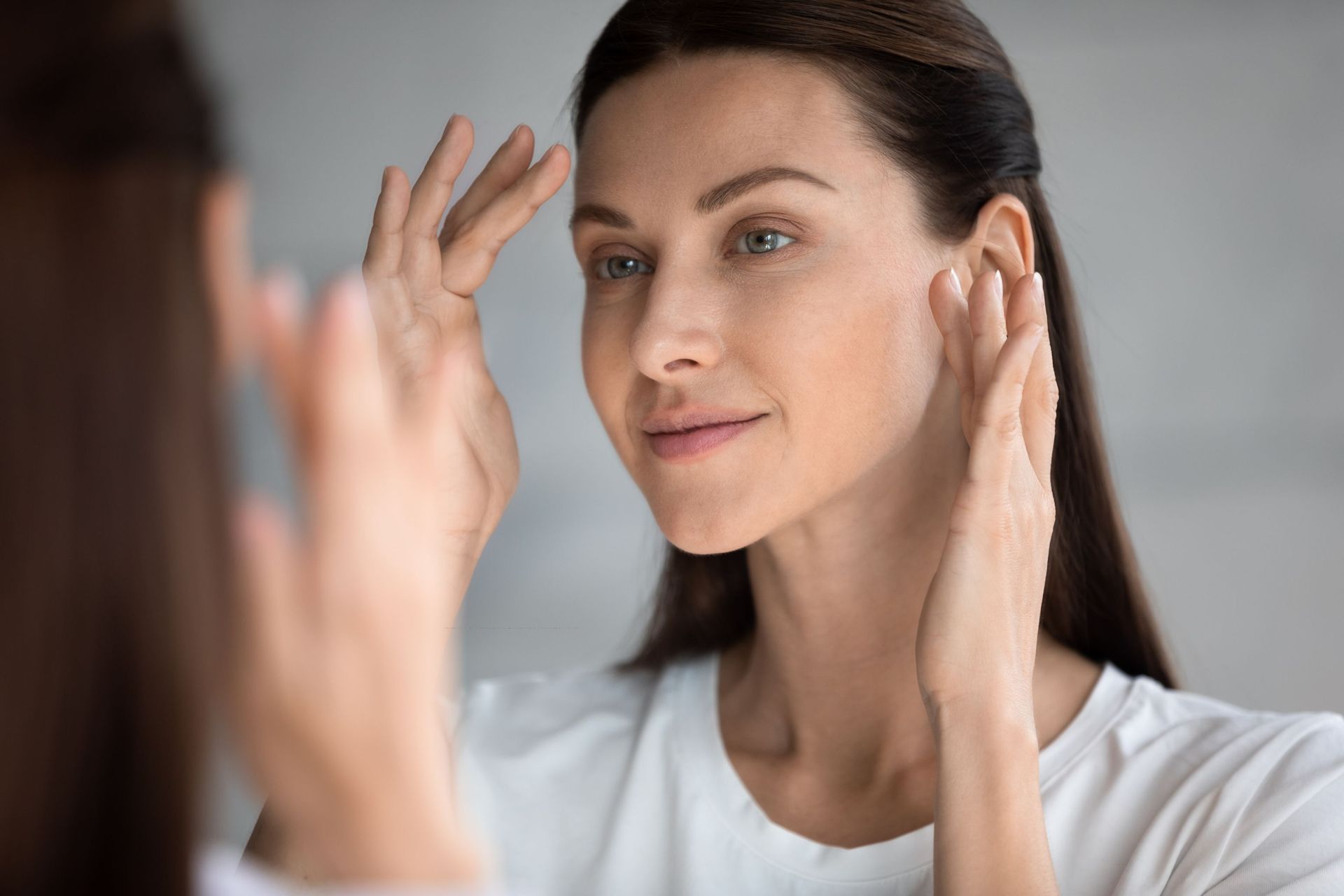 A woman is sitting at a table looking at herself in a mirror.