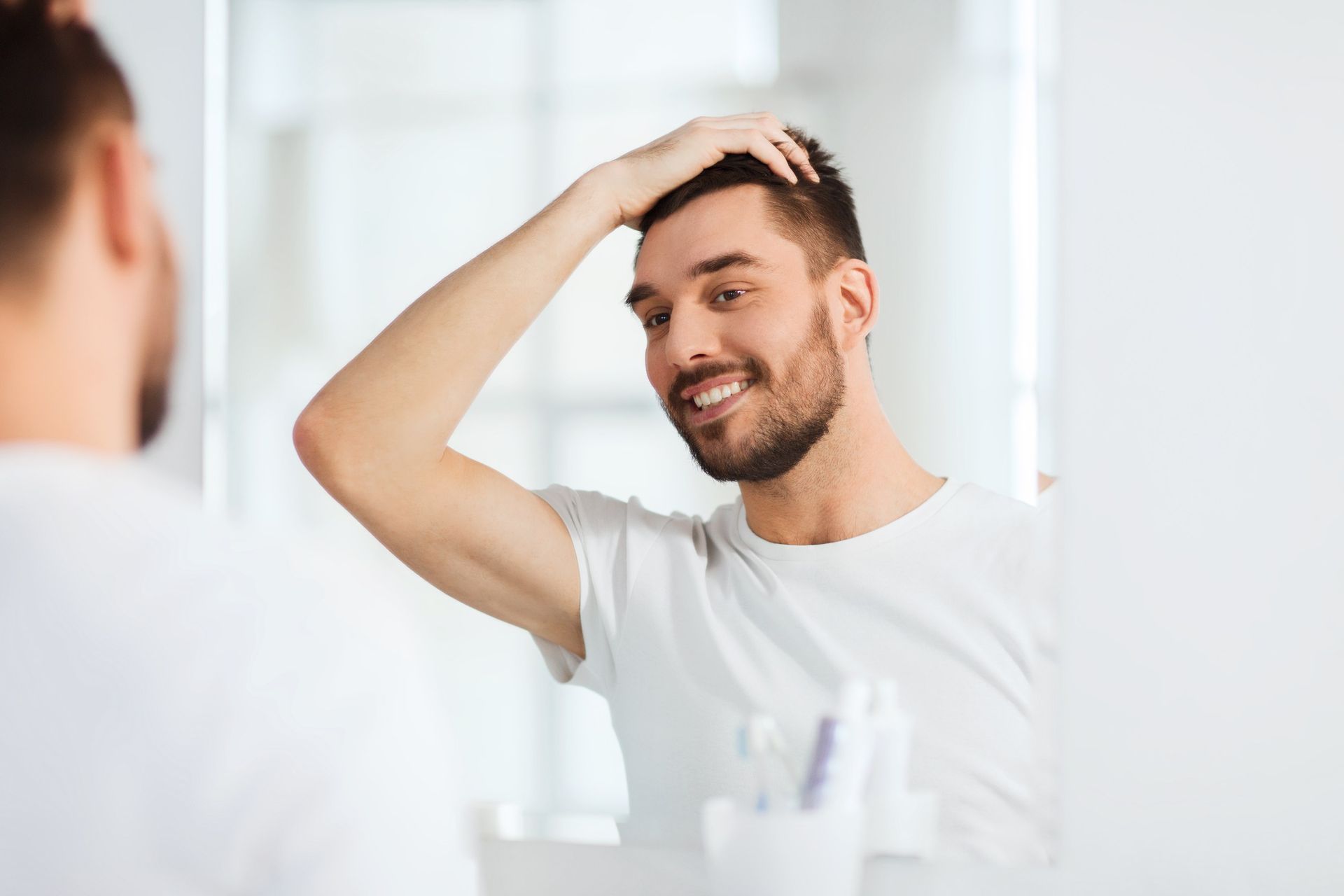 A man is looking at his hair in the mirror.