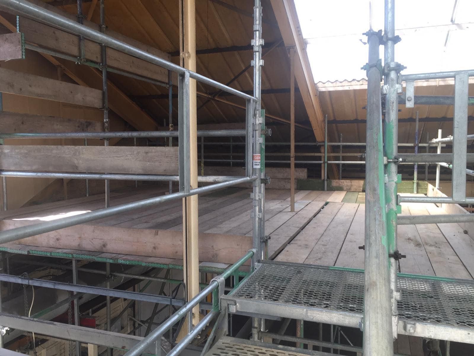 Interior view of a building under construction, with scaffolding, exposed beams, and a worker.