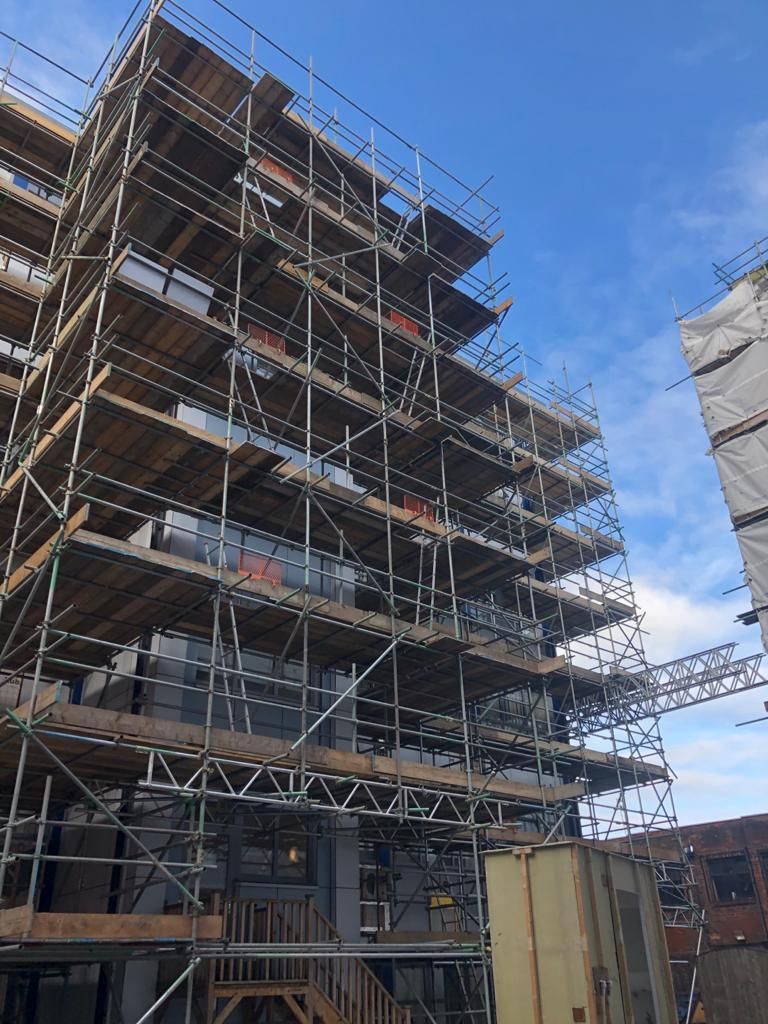 Scaffolding surrounds a multi-story building under construction; blue sky in the background.