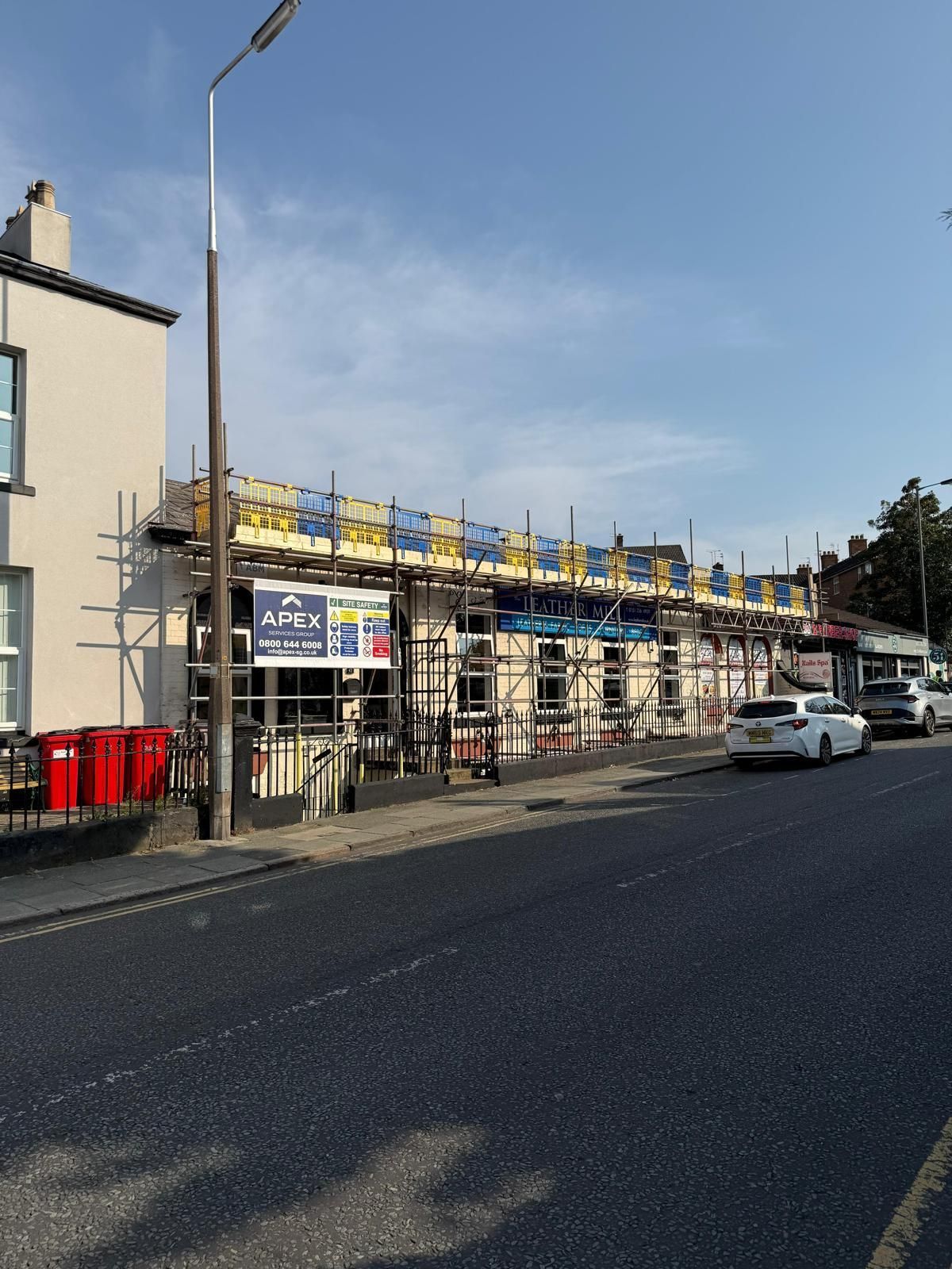 Building under construction with scaffolding. Street view, beige exterior, blue sky.