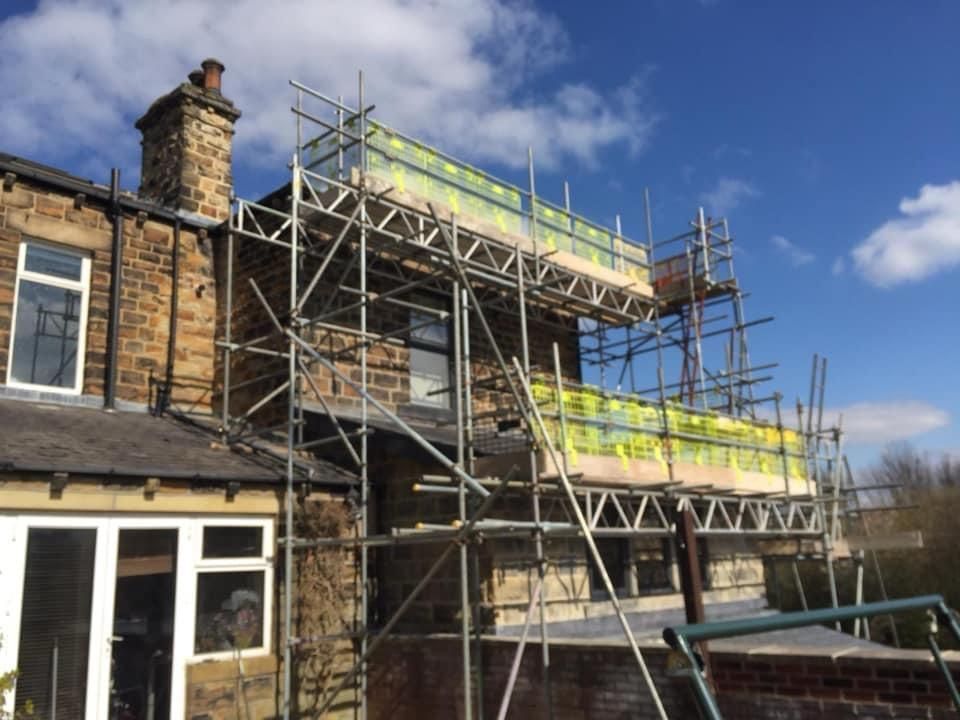 Scaffolding on a stone building, possibly for construction or repair, against a blue sky.
