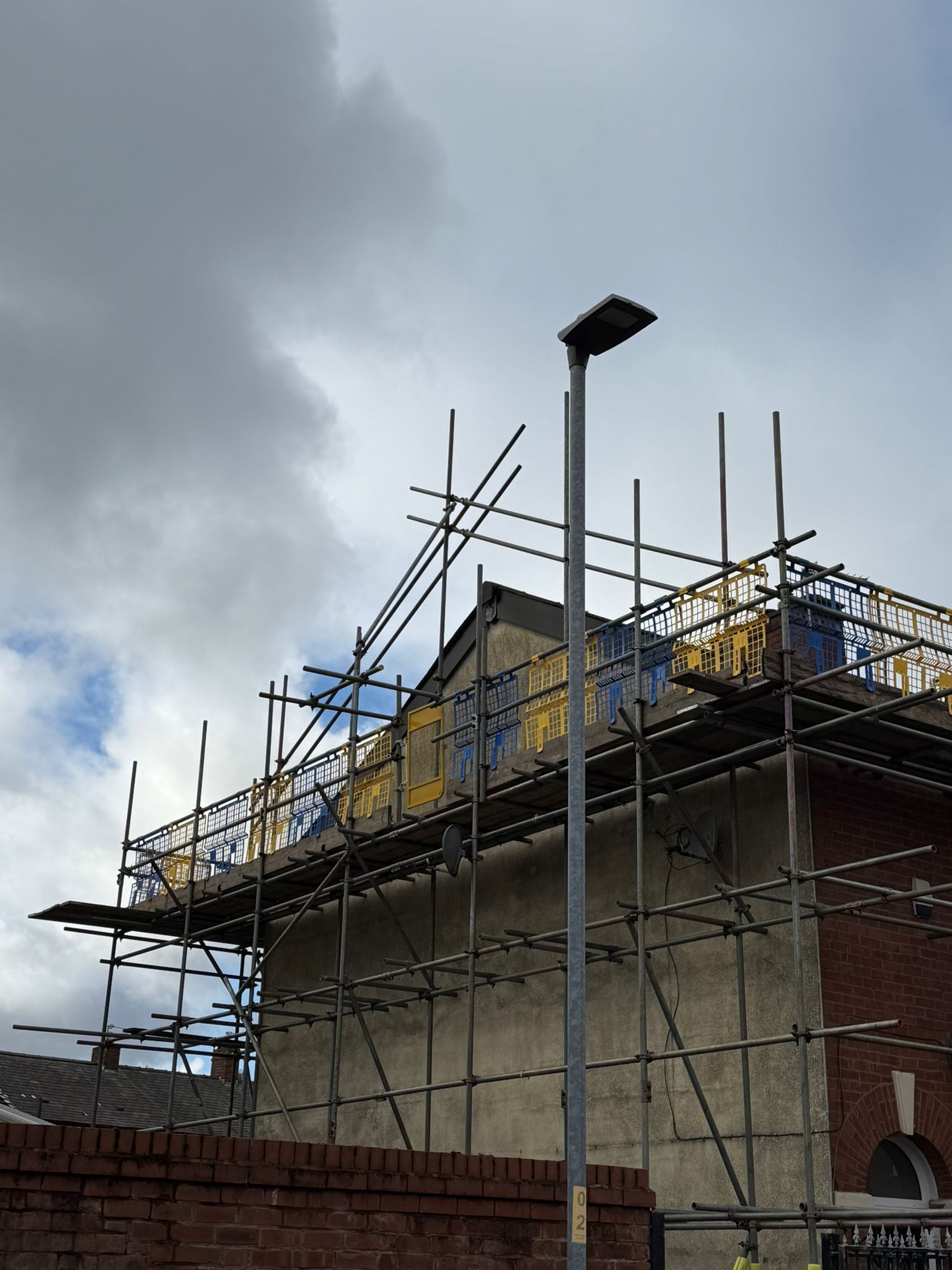 Building under construction with scaffolding against a cloudy sky.
