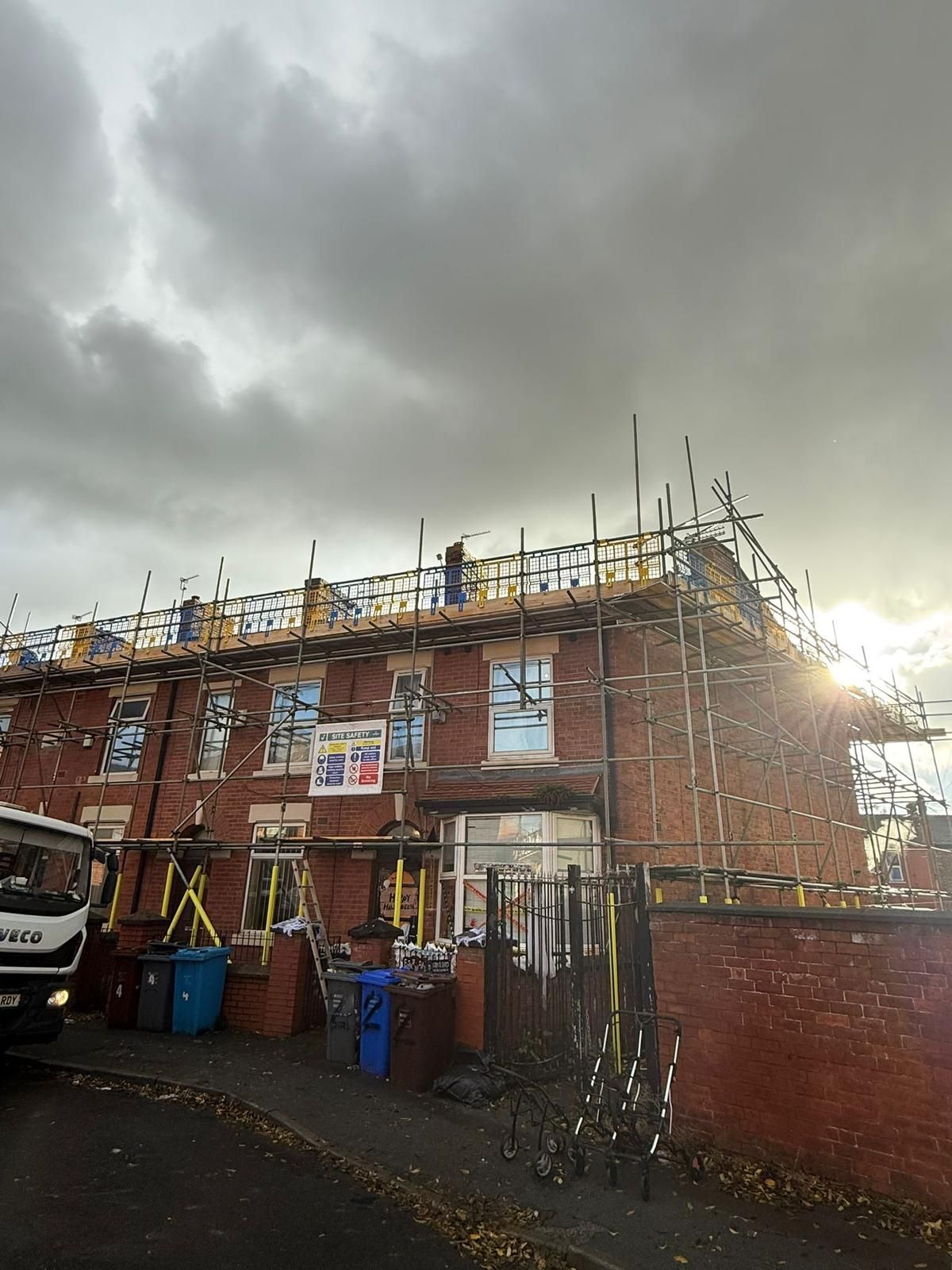 Brick building under renovation; scaffolding surrounds structure. Cloudy sky overhead.