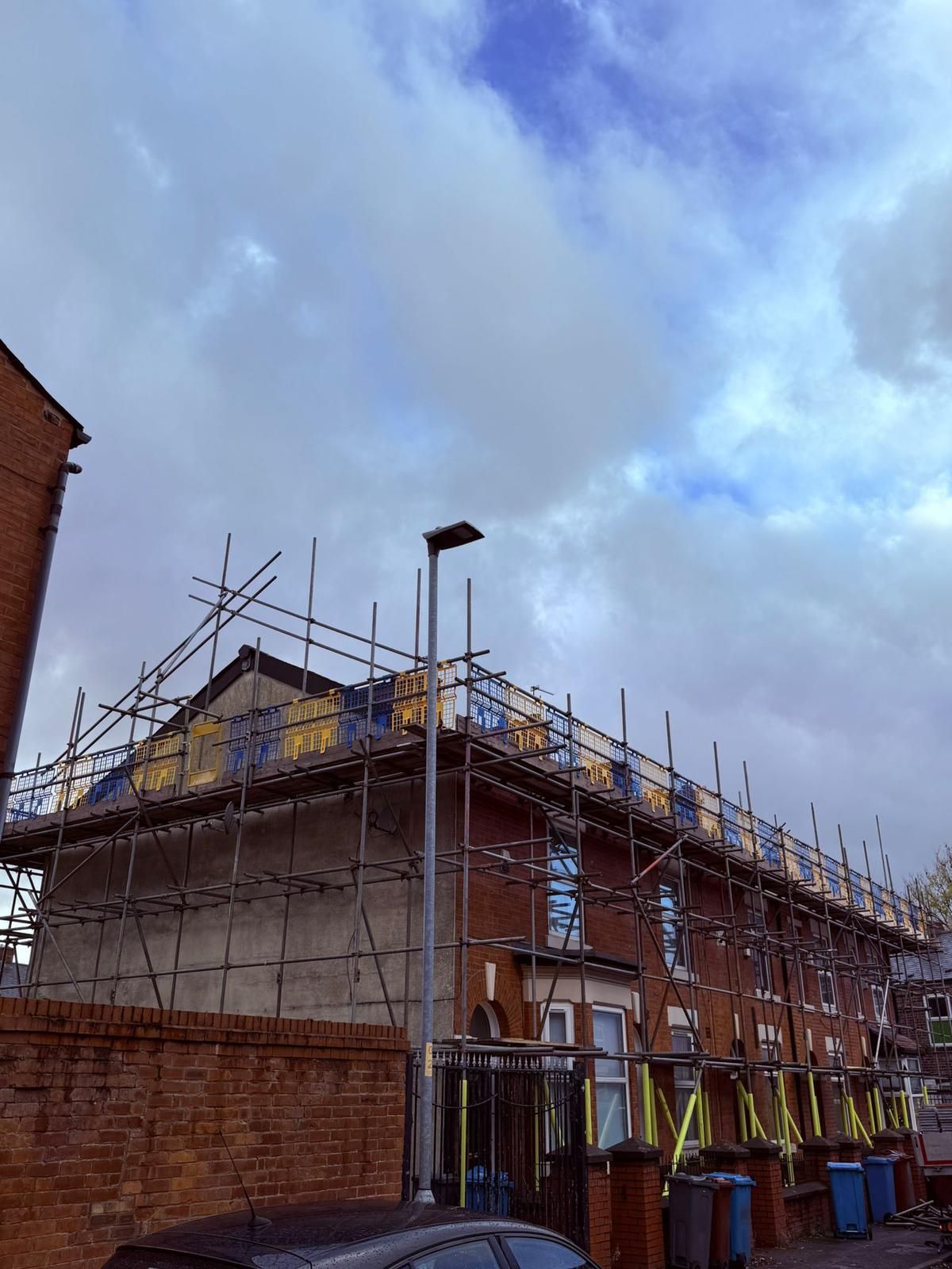 Row houses under construction, covered in scaffolding, against a cloudy sky.
