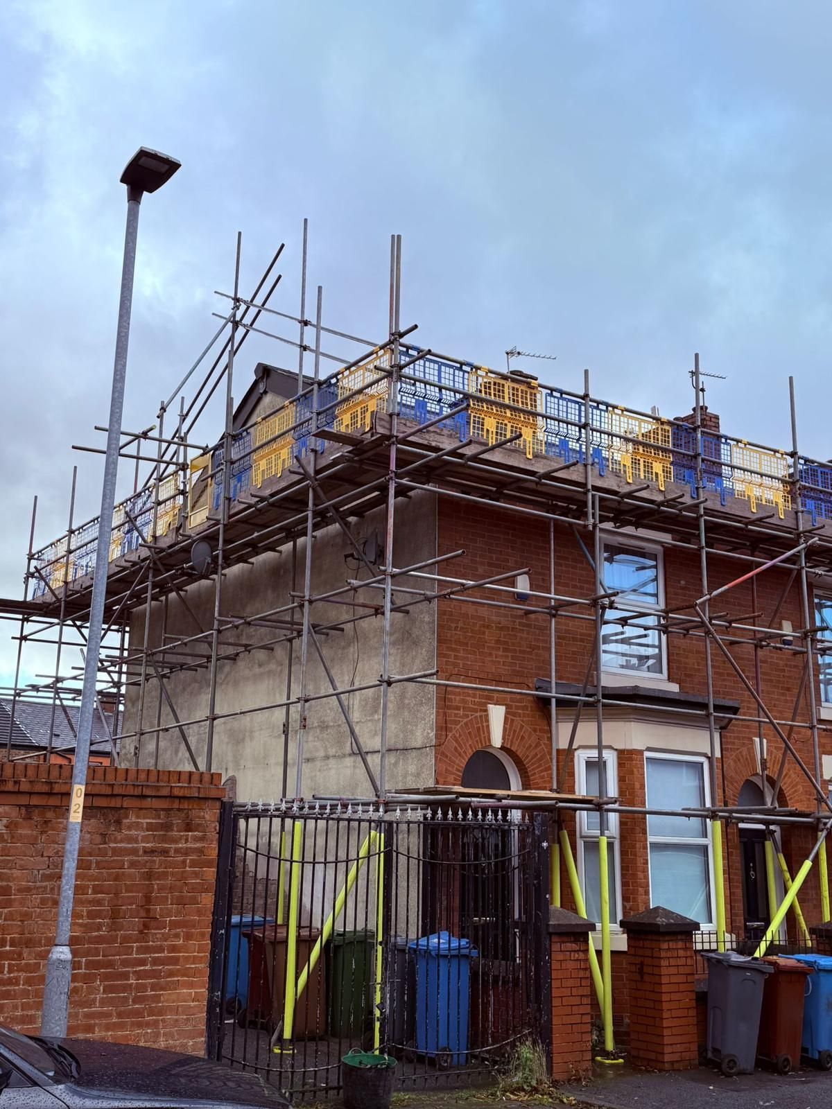 Brick building under construction, scaffolding surrounding the structure, cloudy sky overhead.