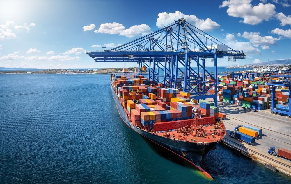 Cargo ship being loaded with containers at a port under a bright blue sky.