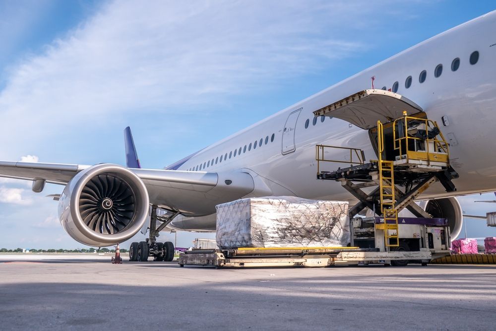 Cargo plane being loaded with a large package on the tarmac under a blue sky.