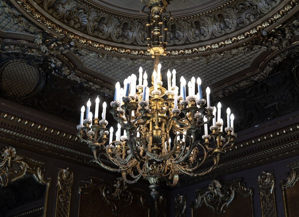 Ornate golden chandelier hangs from a decorated ceiling.