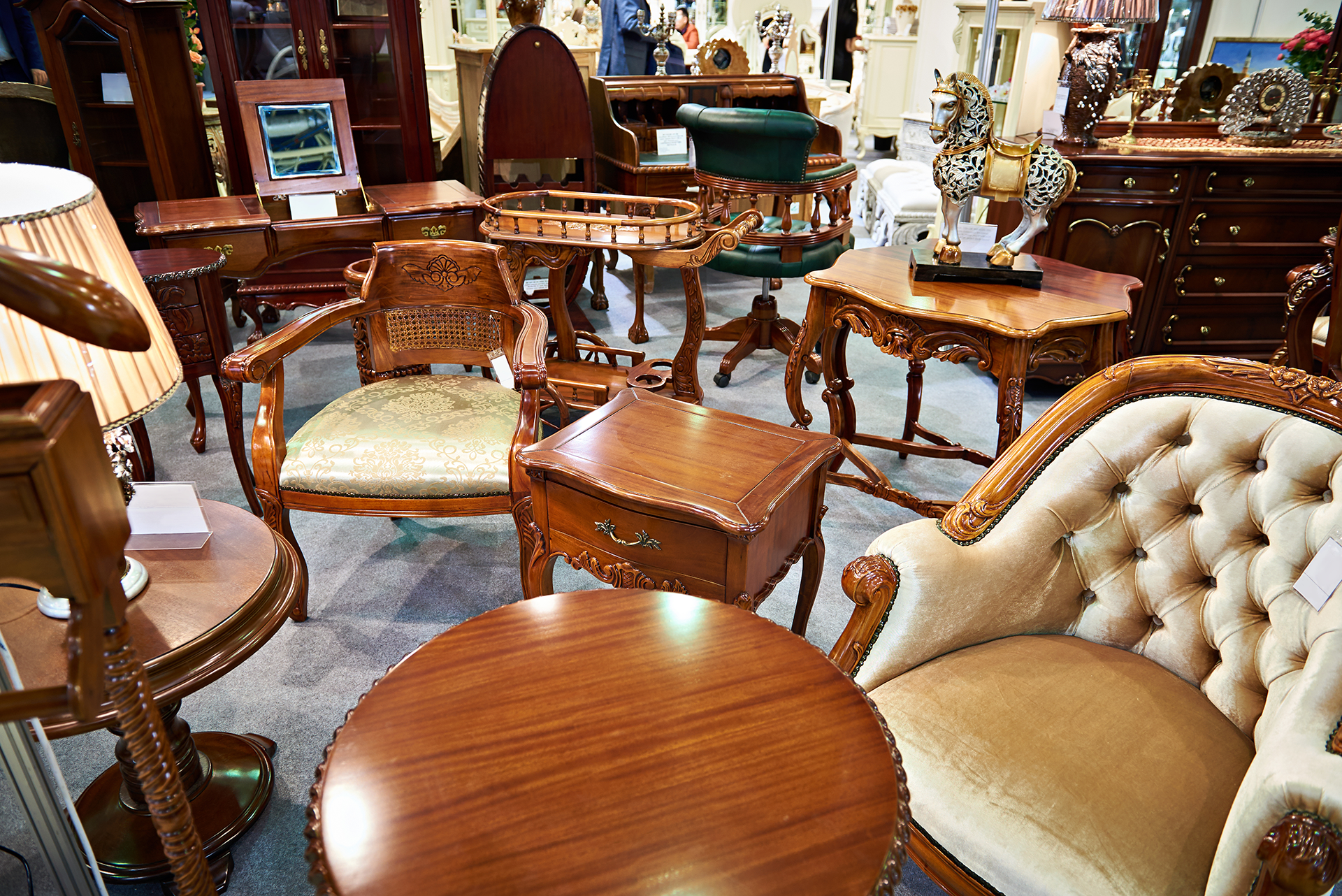 Various antique wooden furniture pieces in a showroom: chairs, tables, dressers. Warm tones.