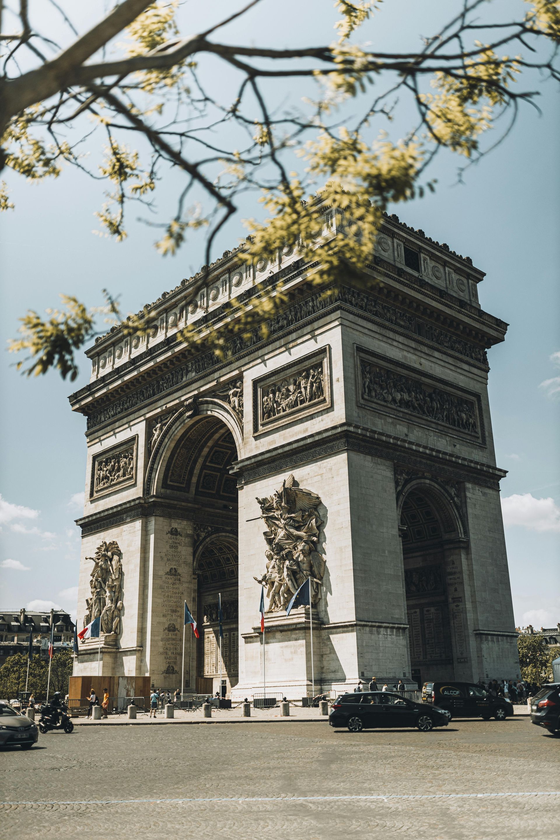 Arc de Triomphe in Paris, France, framed by tree branches, on a sunny day.