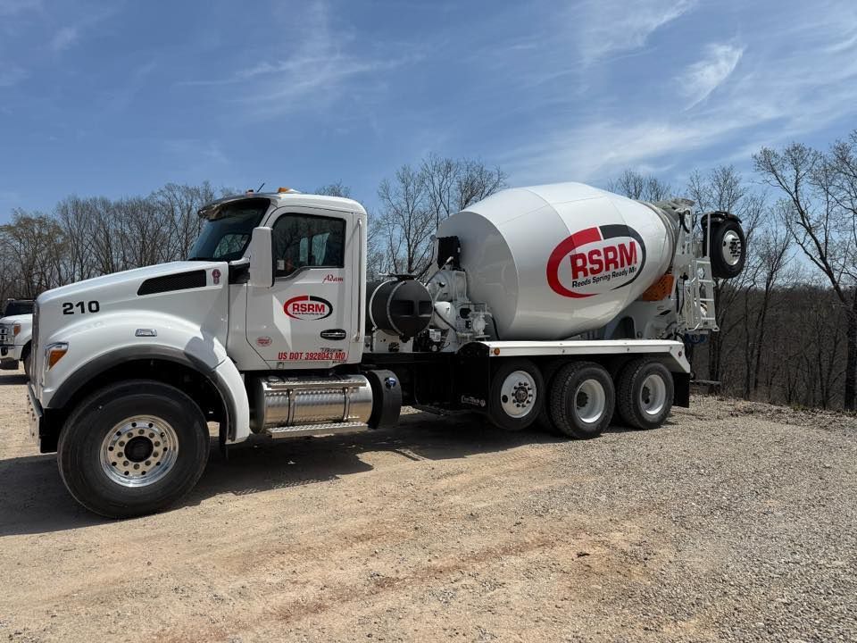 Gray stone retaining wall curves in front of a house, set against a forest and blue sky.