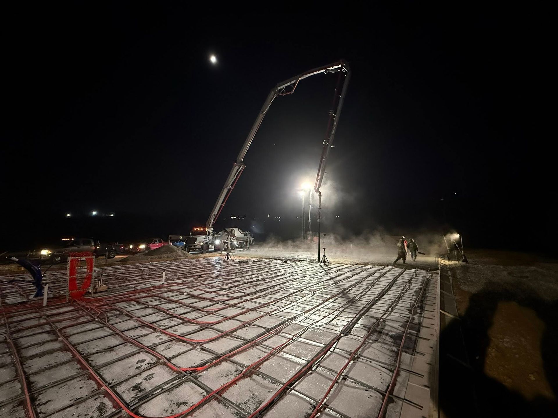 Concrete being poured at night with a pump truck, over in-floor heating tubes.