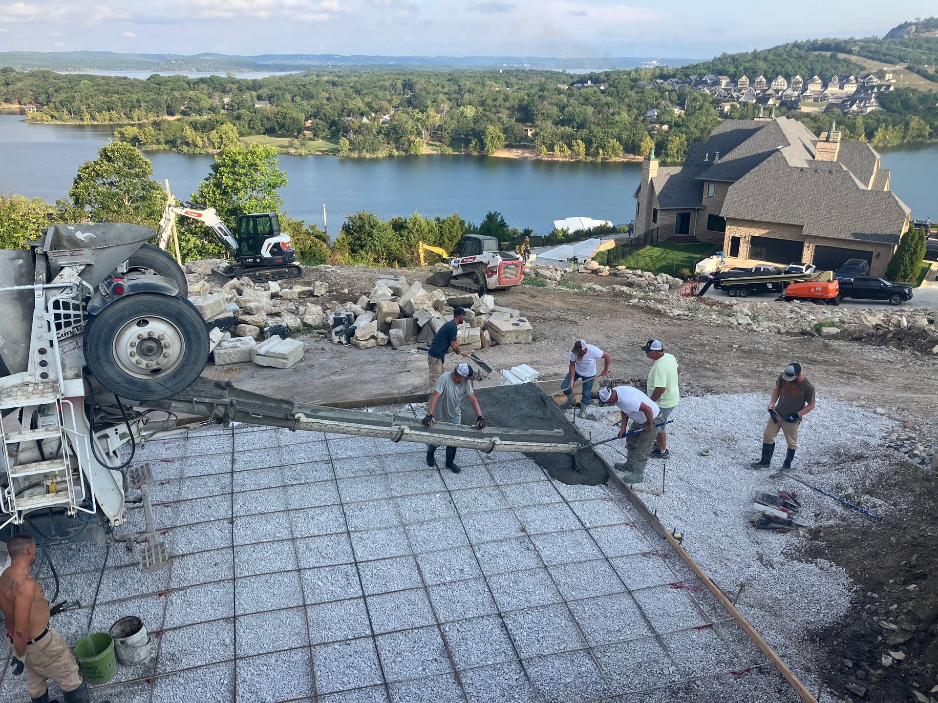 Workers pour concrete for a residential foundational slab by a lake.