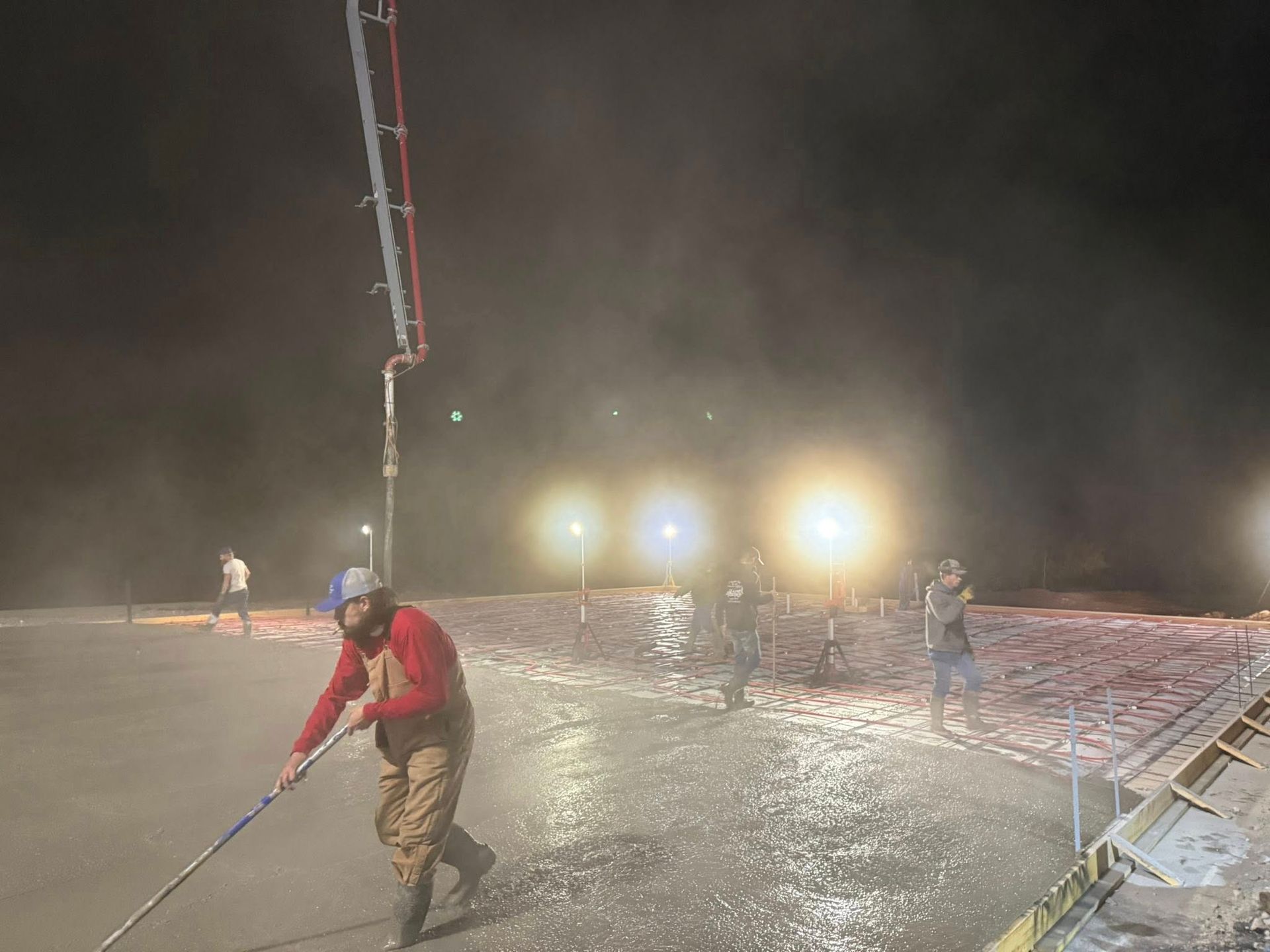 Workers pouring concrete at night, illuminated by bright lights.