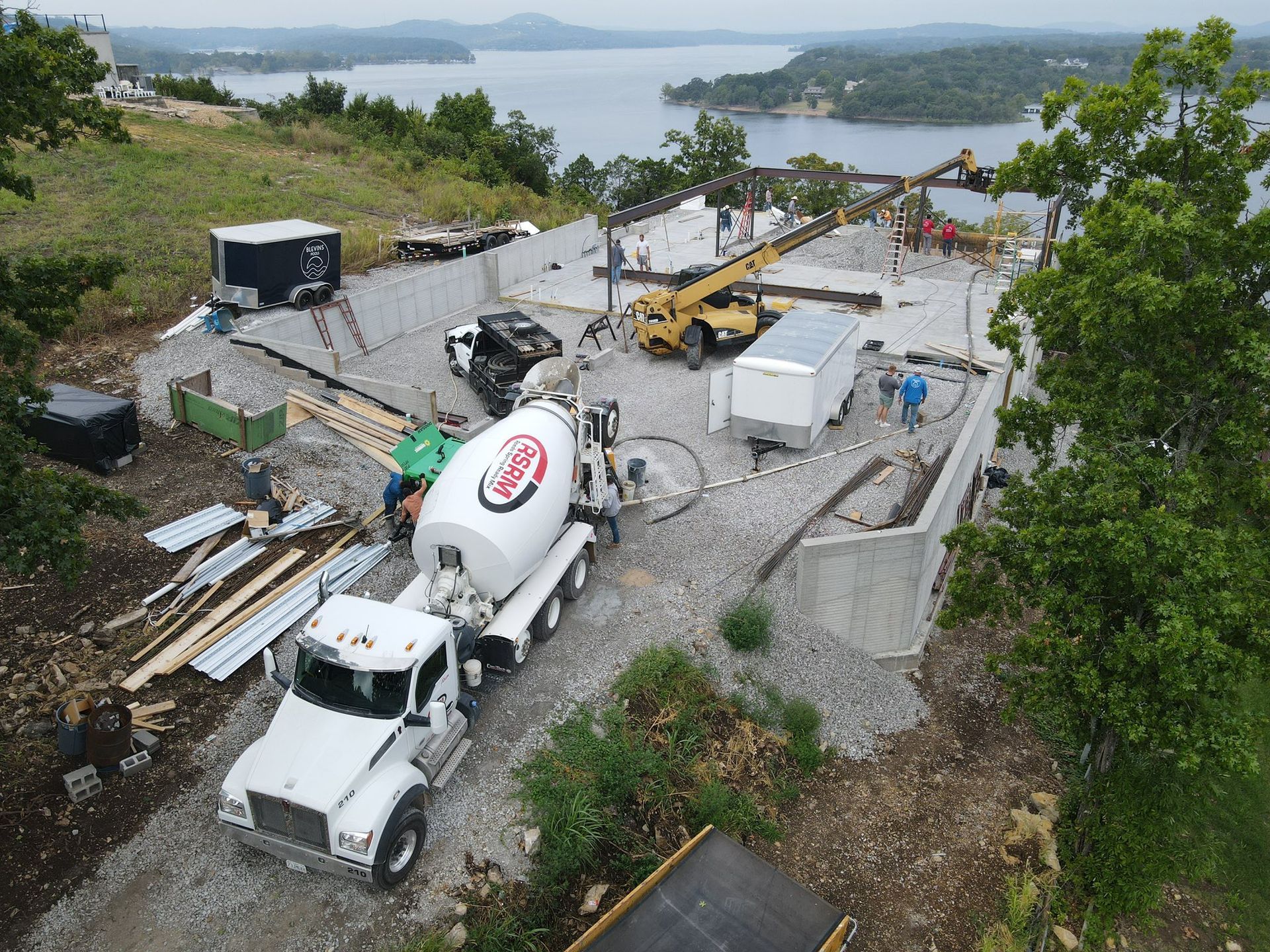 Construction site overlooking a lake; concrete truck, crane, building materials, workers.