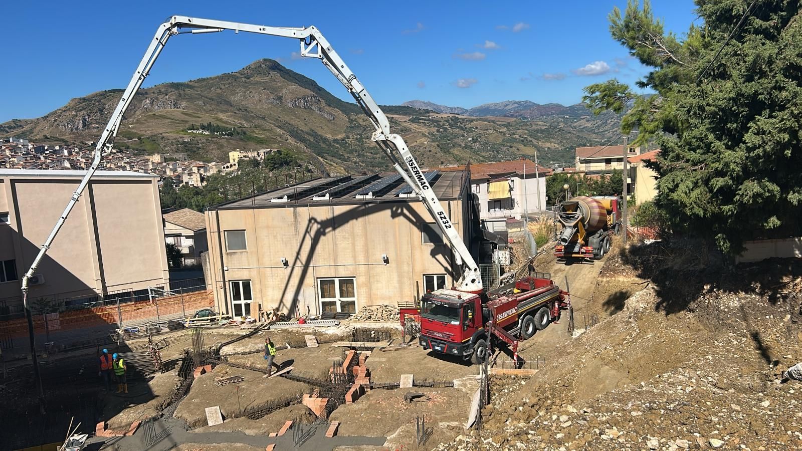 Autobetoniera che versa calcestruzzo in un cantiere edile vicino a edifici e colline.