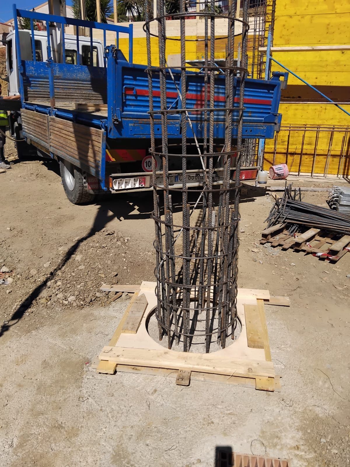 Struttura portante in acciaio rinforzato in un cantiere edile, accanto a un camion blu.