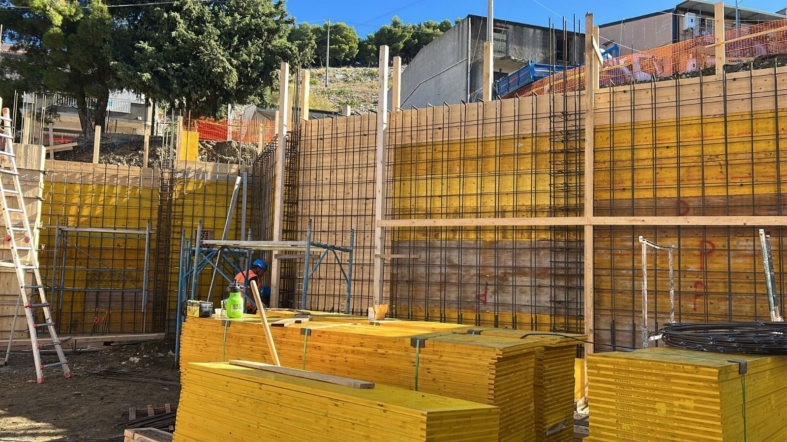 Cantiere con pareti rivestite di pannelli gialli, barre di armatura a vista e supporti in legno.