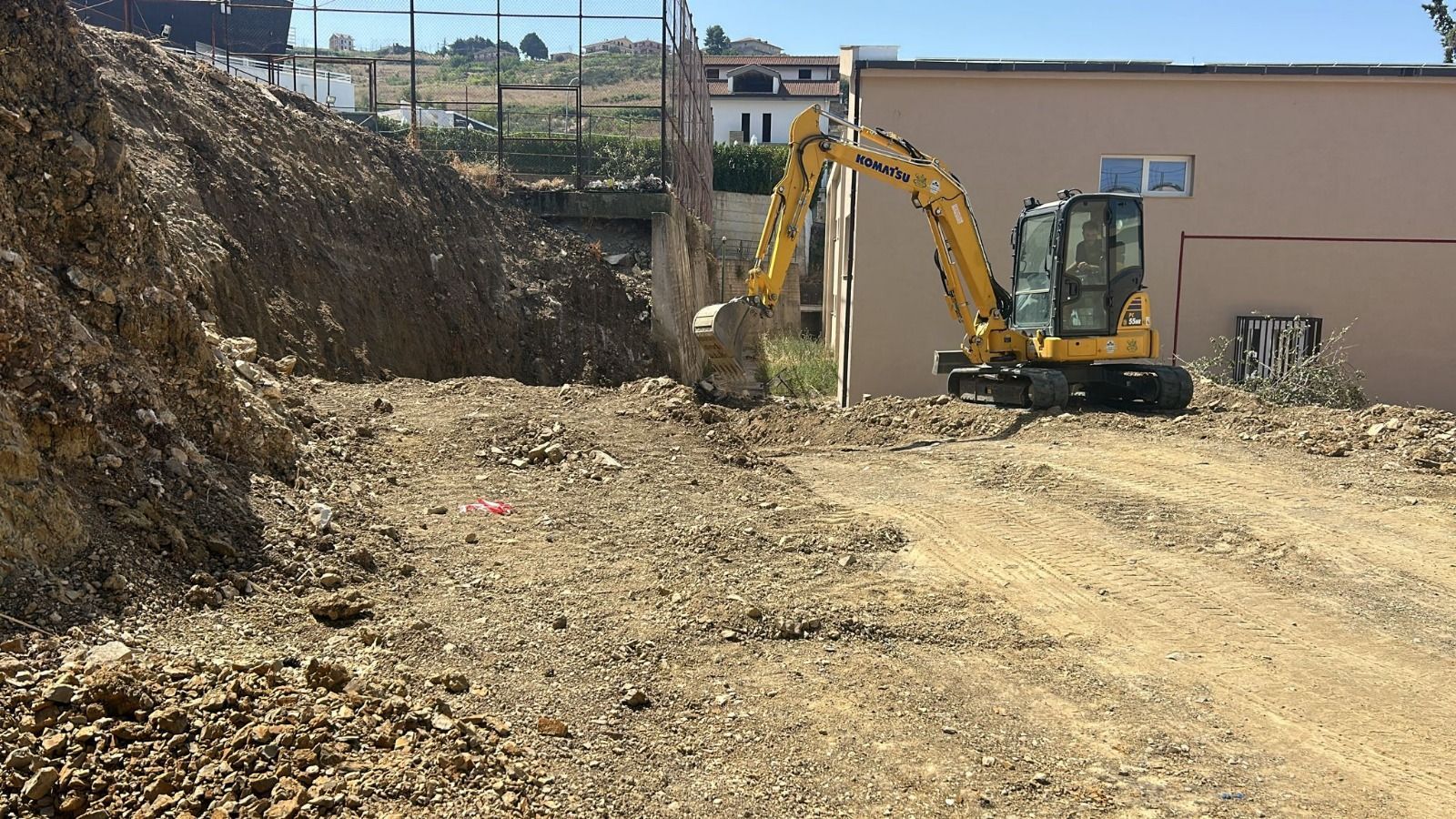 Escavatore giallo che scava in un mucchio di terra e rocce accanto a un edificio.