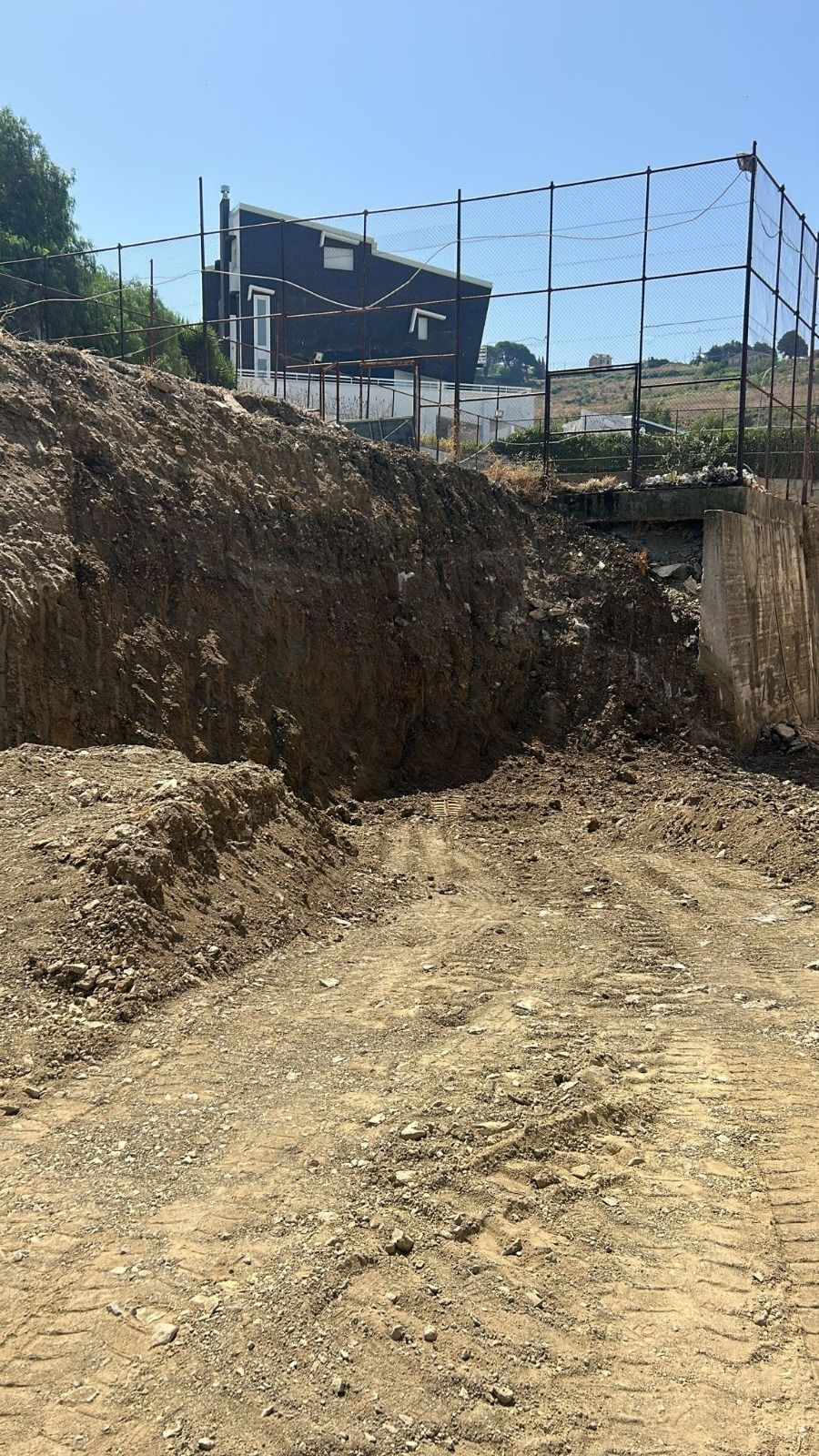 Cumulo di terra e ghiaia con un edificio sullo sfondo. Area recintata dietro l'edificio.