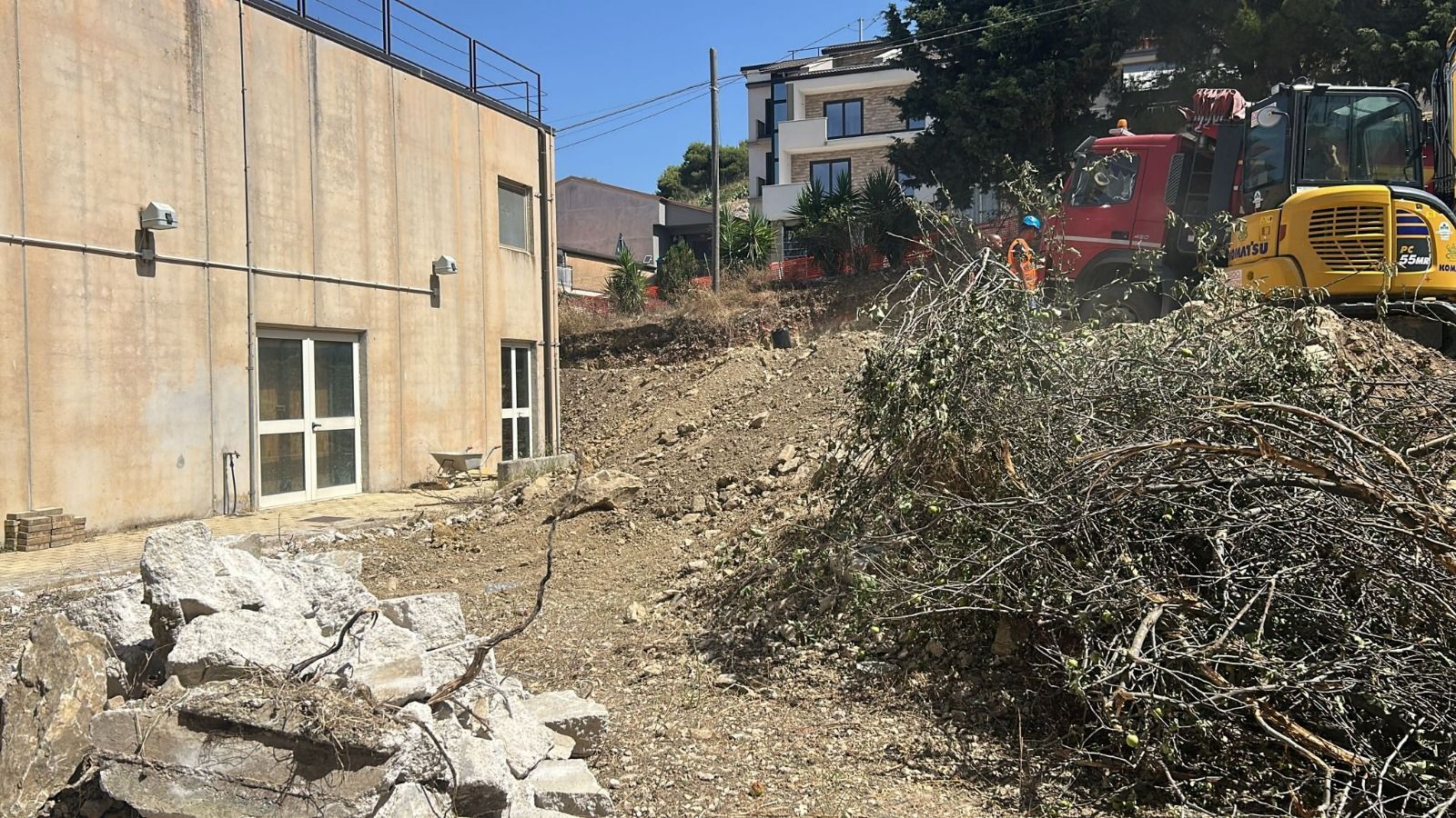 Cantiere con un edificio, un escavatore e terreno sradicato.