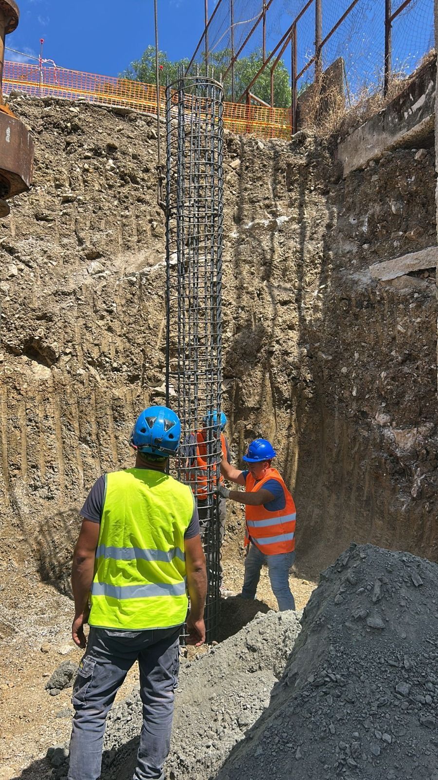 Gli operai edili con i caschi protettivi installano una gabbia di barre d'armatura nella trincea scavata.