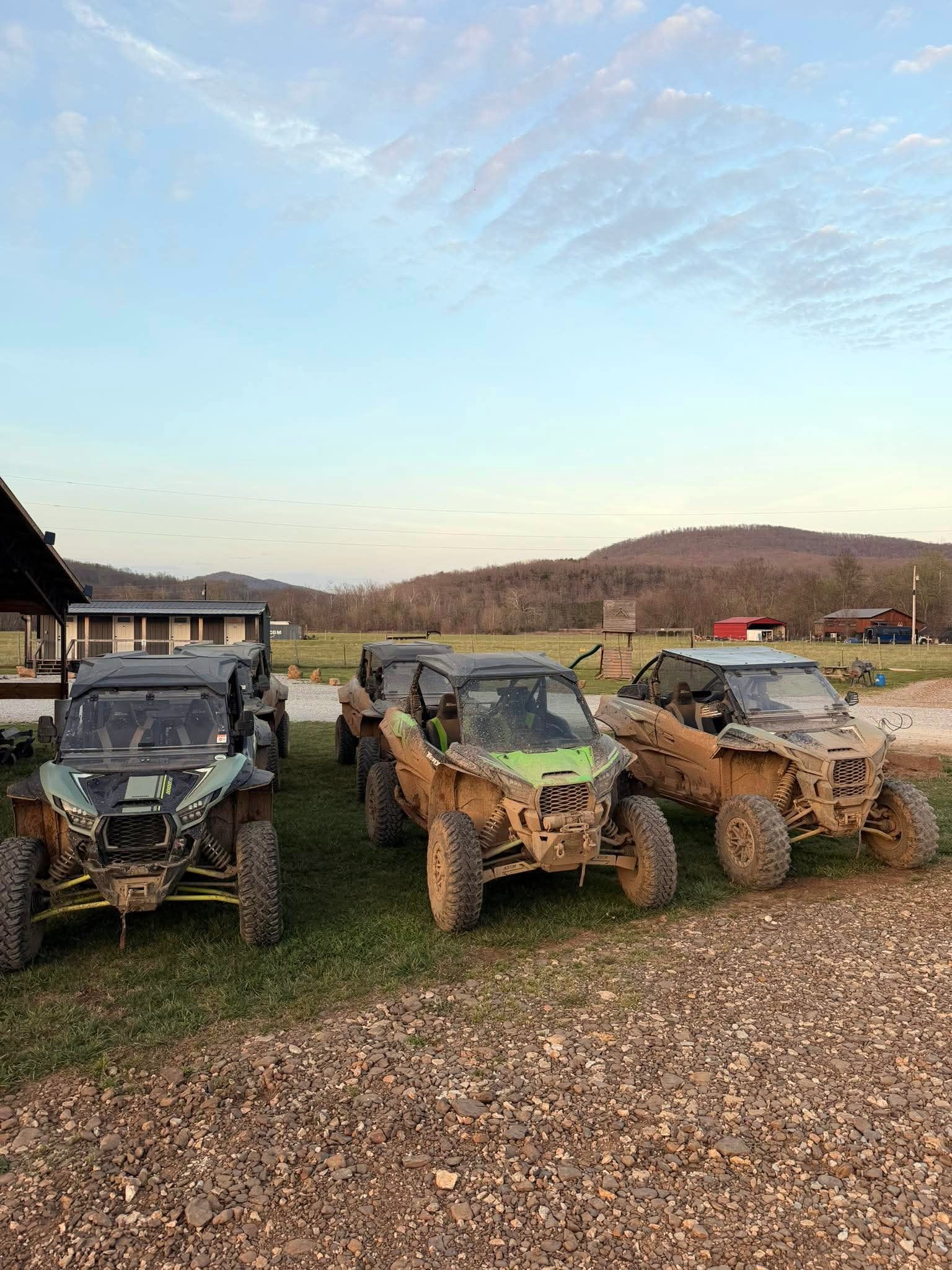 Three off-road buggies parked on grass and gravel under a cloudy sky near a rural building.