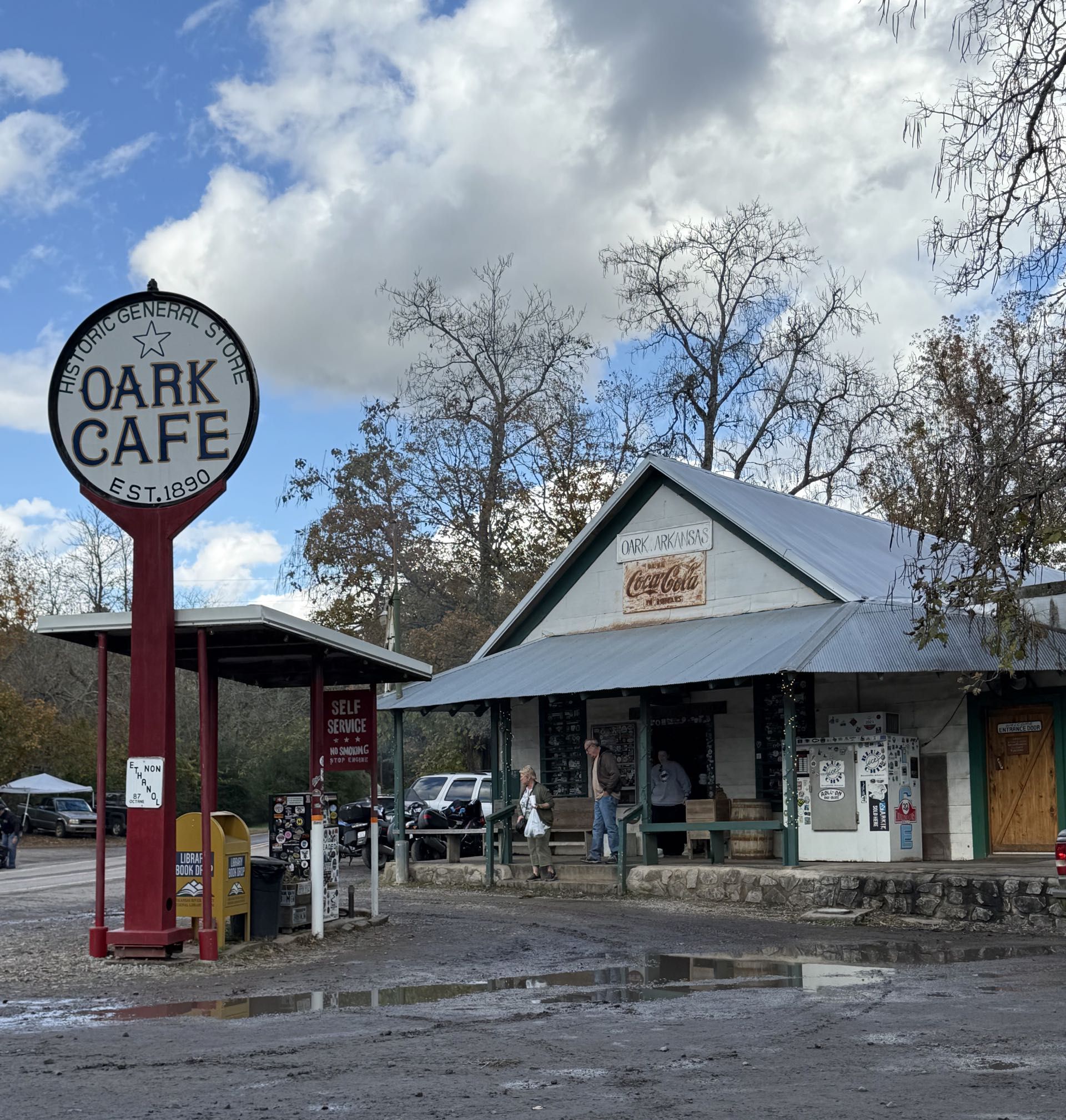 Oark Cafe, a rustic building with a metal roof and large sign, stands under a cloudy sky with people near the entrance.