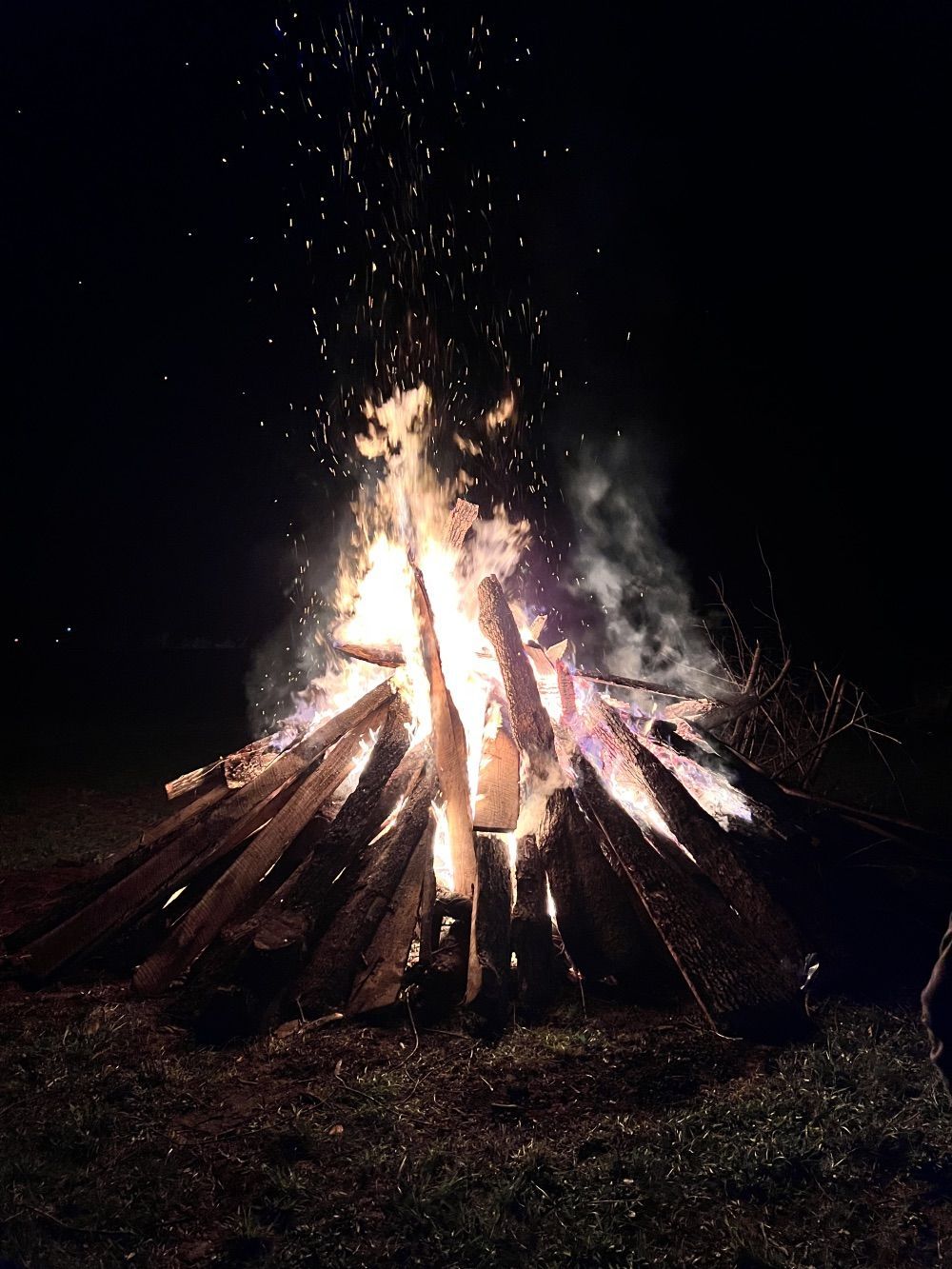 Large bonfire burning at night, with sparks and smoke rising into the dark sky.