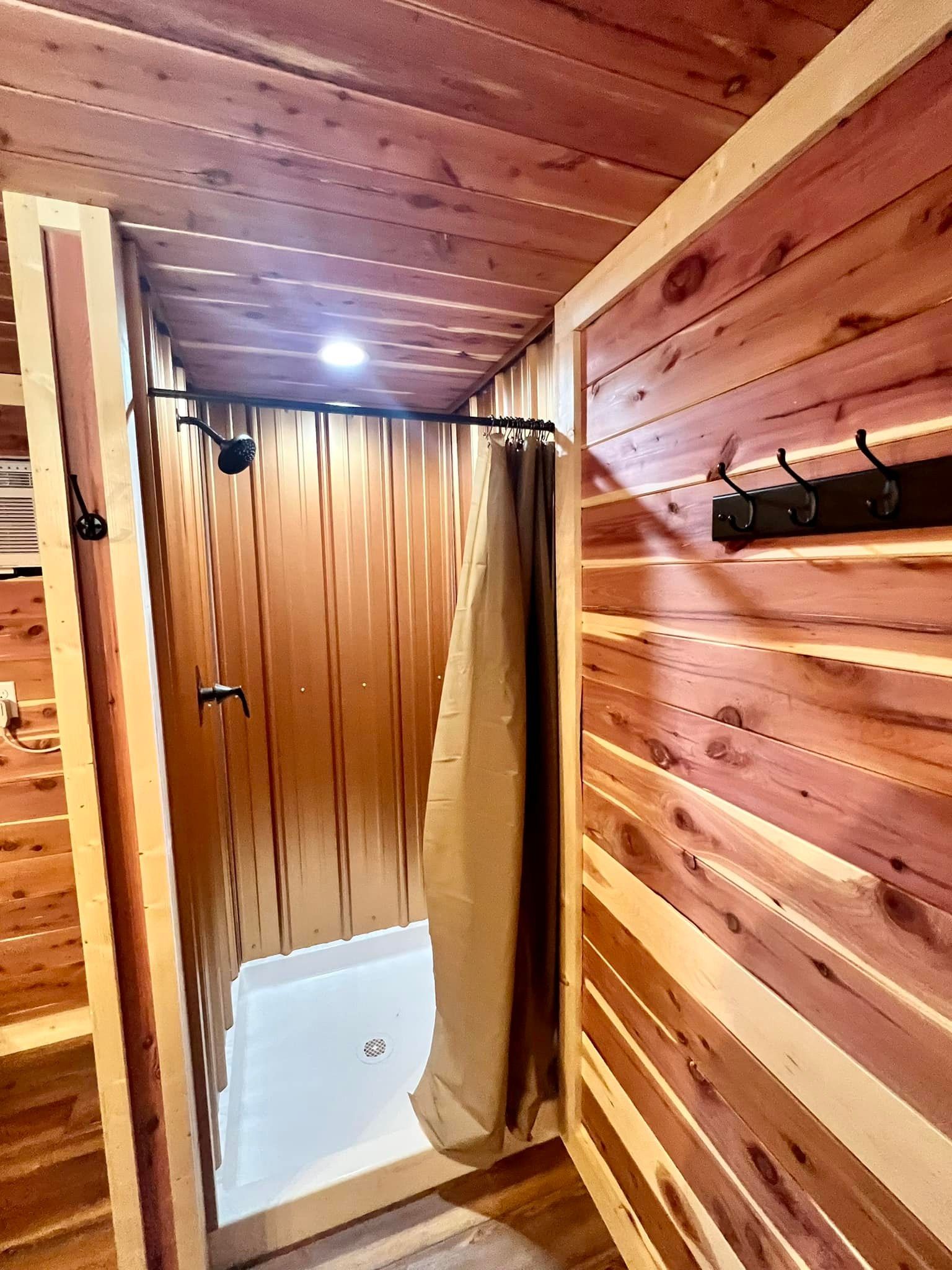 Wood-paneled shower stall with a curtain, white shower base, and a lit wooden hallway.
