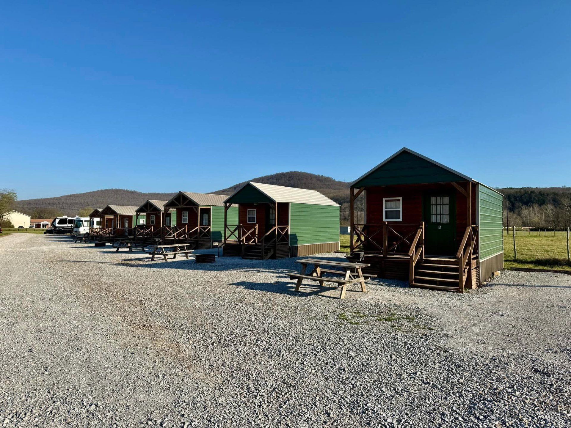 Row of small cabin-like sheds on gravel under a clear blue sky, with hills in the background